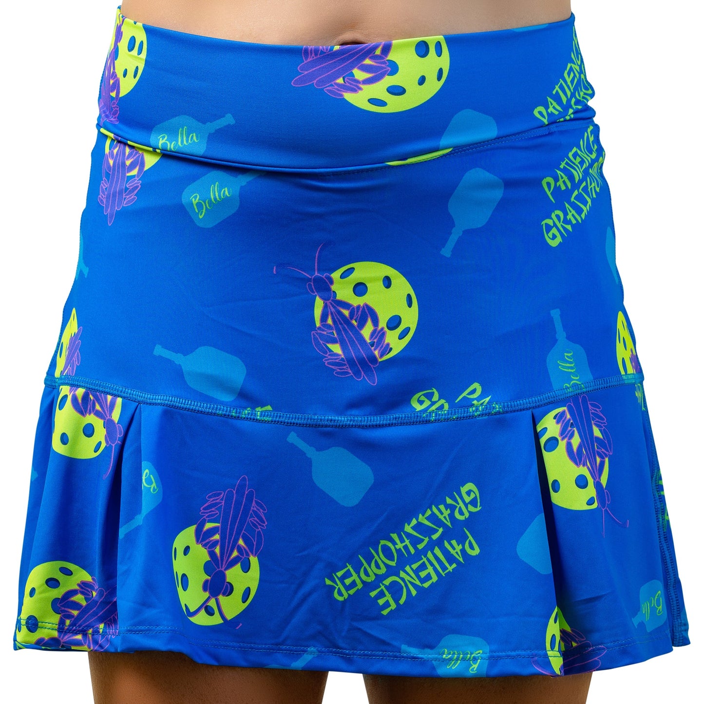 A woman wears the Pickleball Bella PB Drop Pleat Skort Patience Grasshopper, a blue pickleball skirt made from 4-way stretch fabric.
