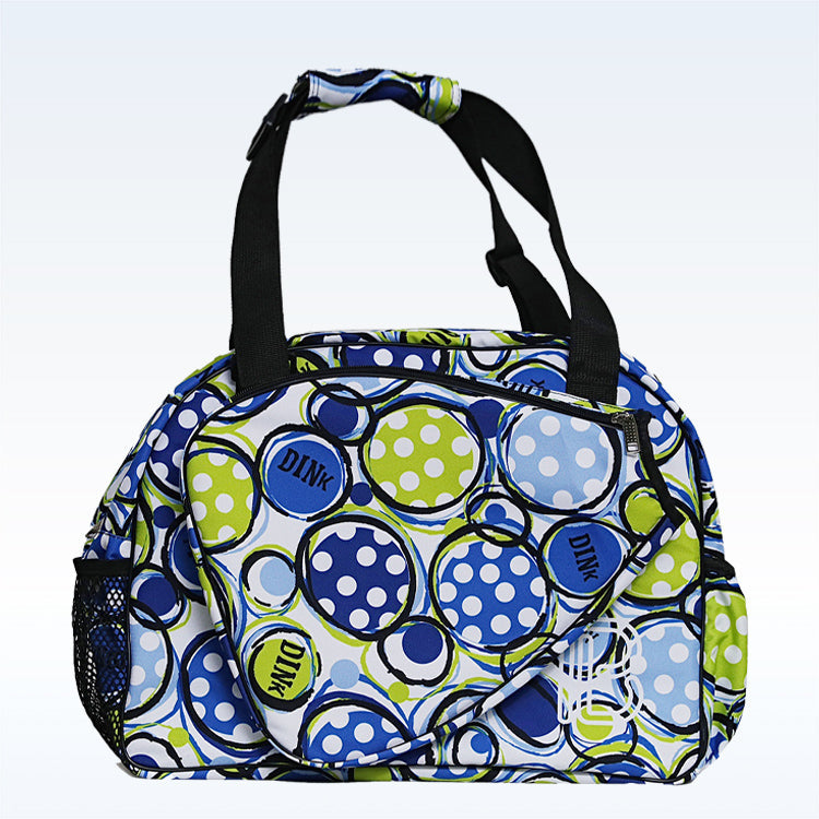 The Pickleball Bella PB Duffle Bag Dink 1 showcases blue, green, and white polka dots—some with "DINK." It features black handles, a mesh side pocket, and a large front zippered paddle pocket in the same playful print.