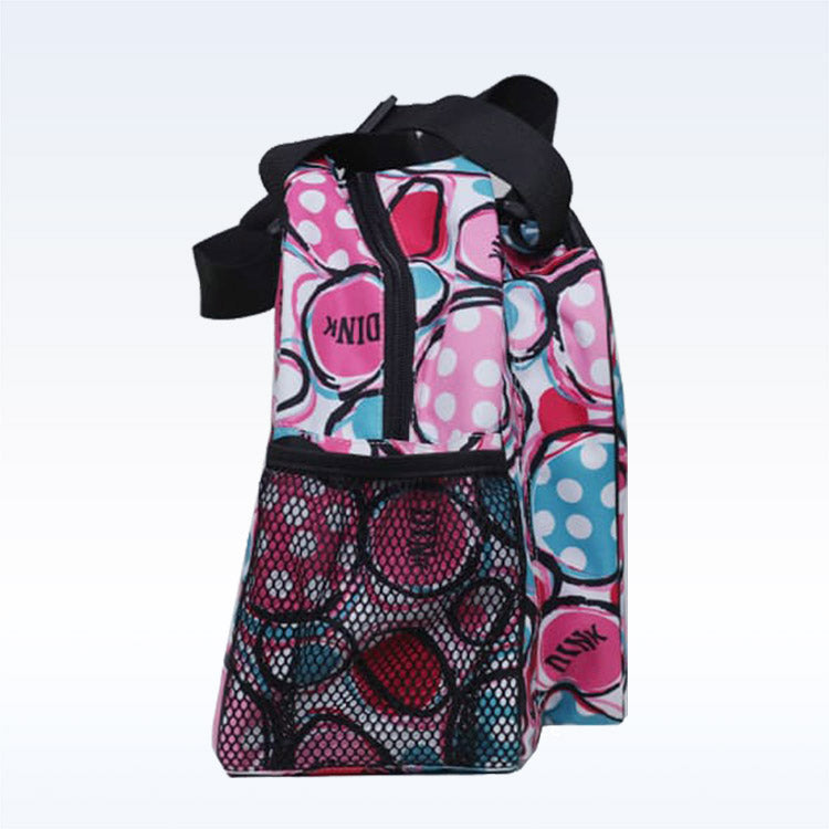 The Pickleball Bella "c" is a colorful tote bag with a black zipper and handle, featuring pink, blue, and white bubble patterns, a black mesh front pocket, and “PINK” printed on the fabric—perfect as a pickleball duffle bag.