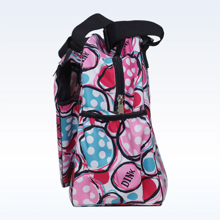 The Pickleball Bella c duffle bag features pink, blue, and white polka-dotted circles with “DINK” on the side. Black handles and a vertical zippered paddle pocket secure your pickleball gear in style.