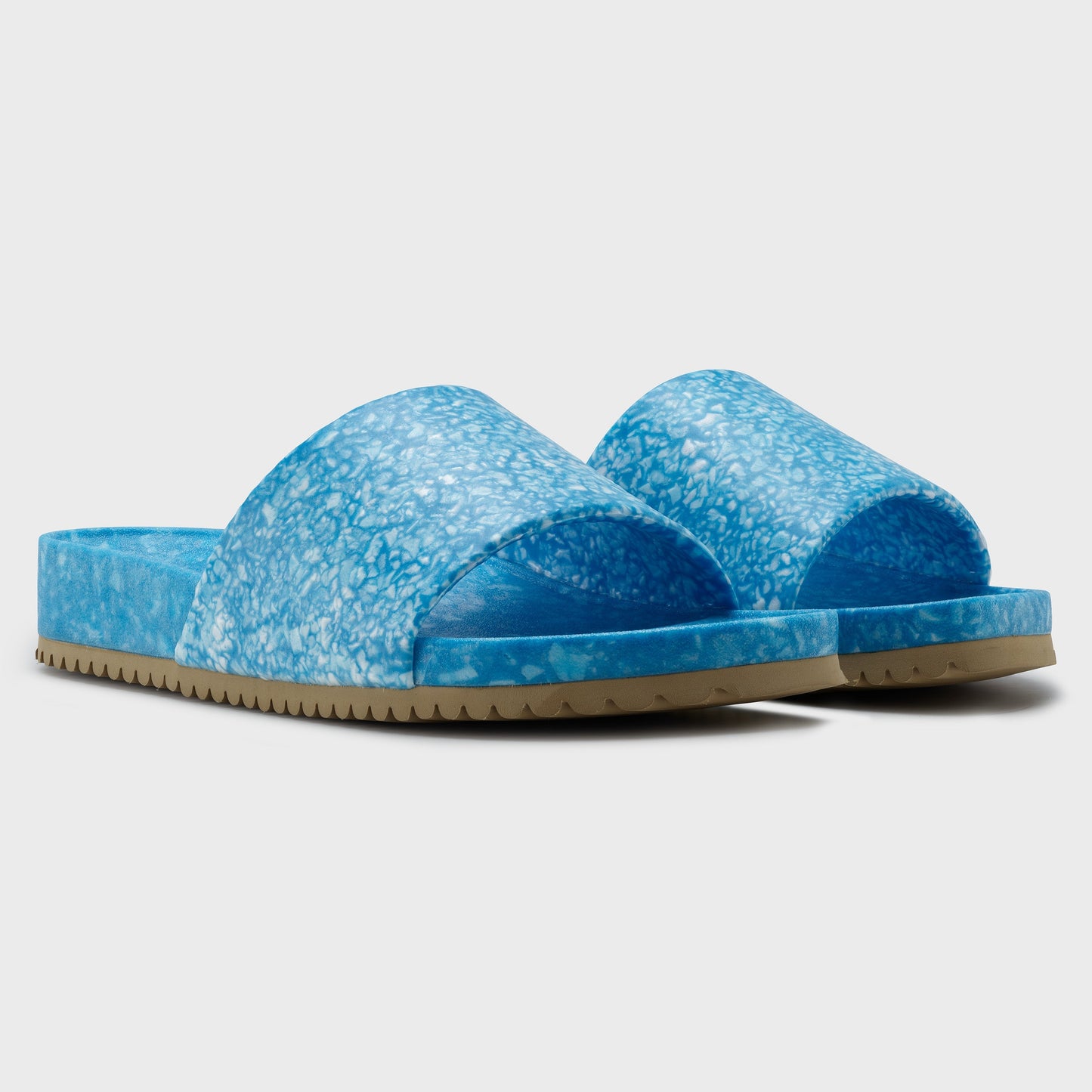 The Blumaka Fleks® East Beach Slide features blue, marbled wide bands and light brown ridged soles for grip and alignment support, shown against a white background.