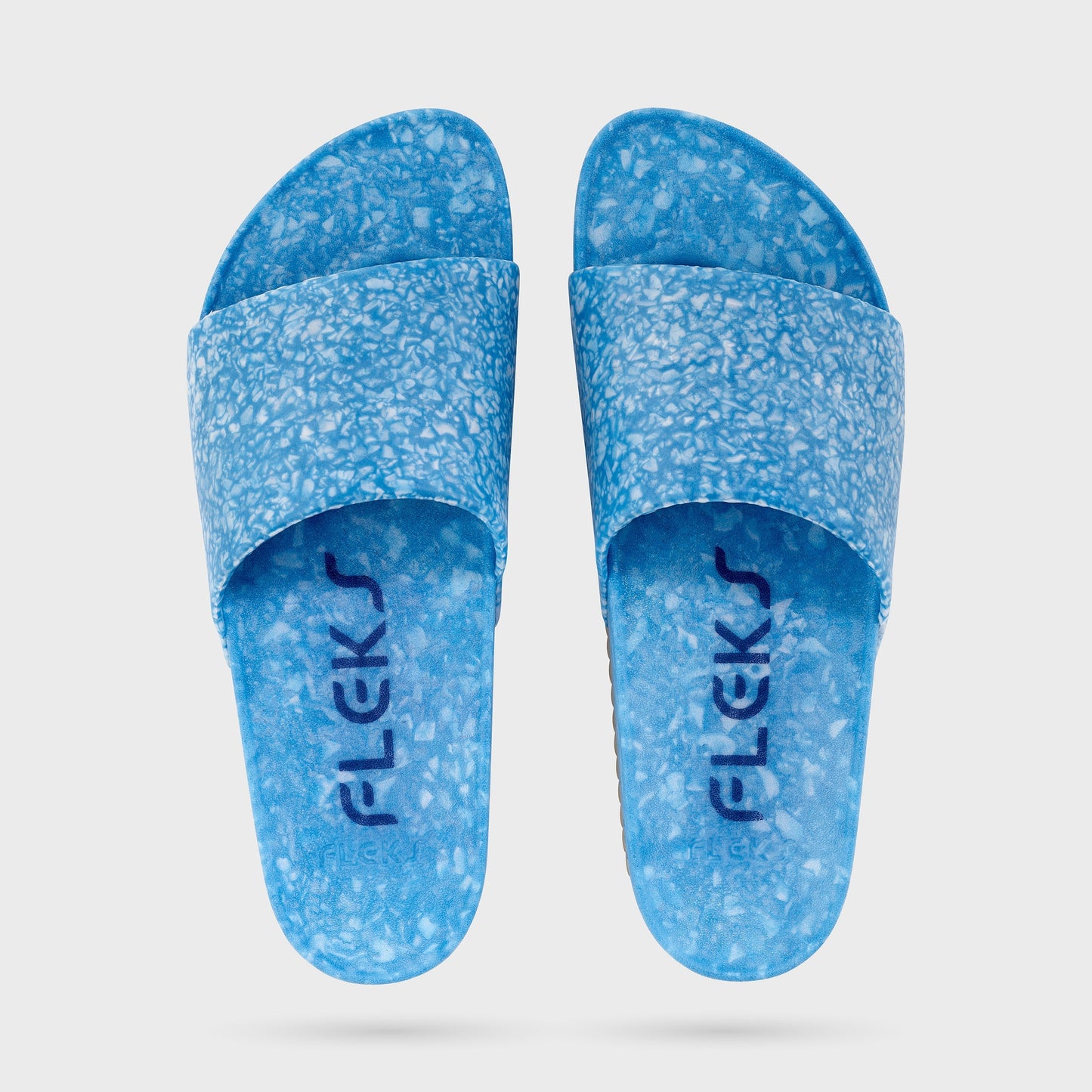 Blumaka Fleks® East Beach Slide sandals feature blue speckled wide straps, a marbled pattern, and supportive design. "FLEKS" is printed in dark blue on the textured footbeds. Sandals shown side by side on a white background.