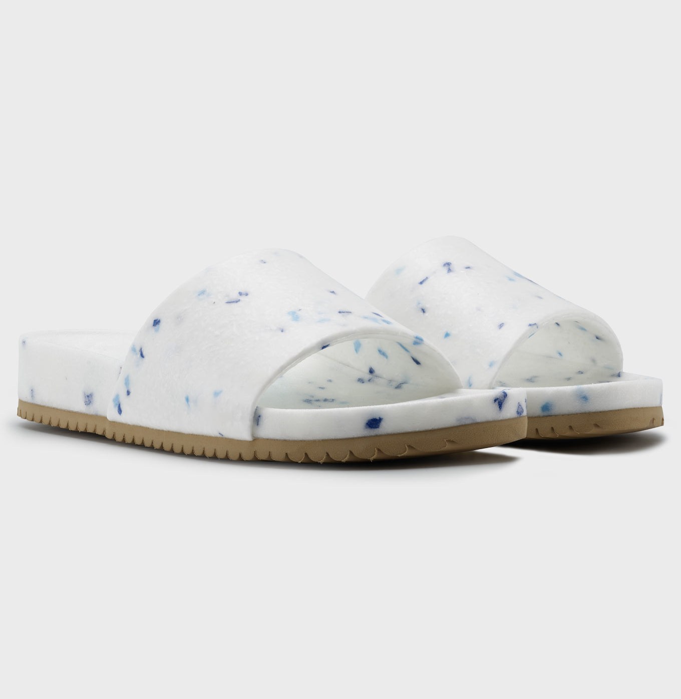 The Blumaka Fleks® East Beach Slide is a white sandal with blue speckles, an open toe, single thick strap, and beige ridged sole for comfort and alignment—ideal for athlete recovery. Shown on a plain white background.