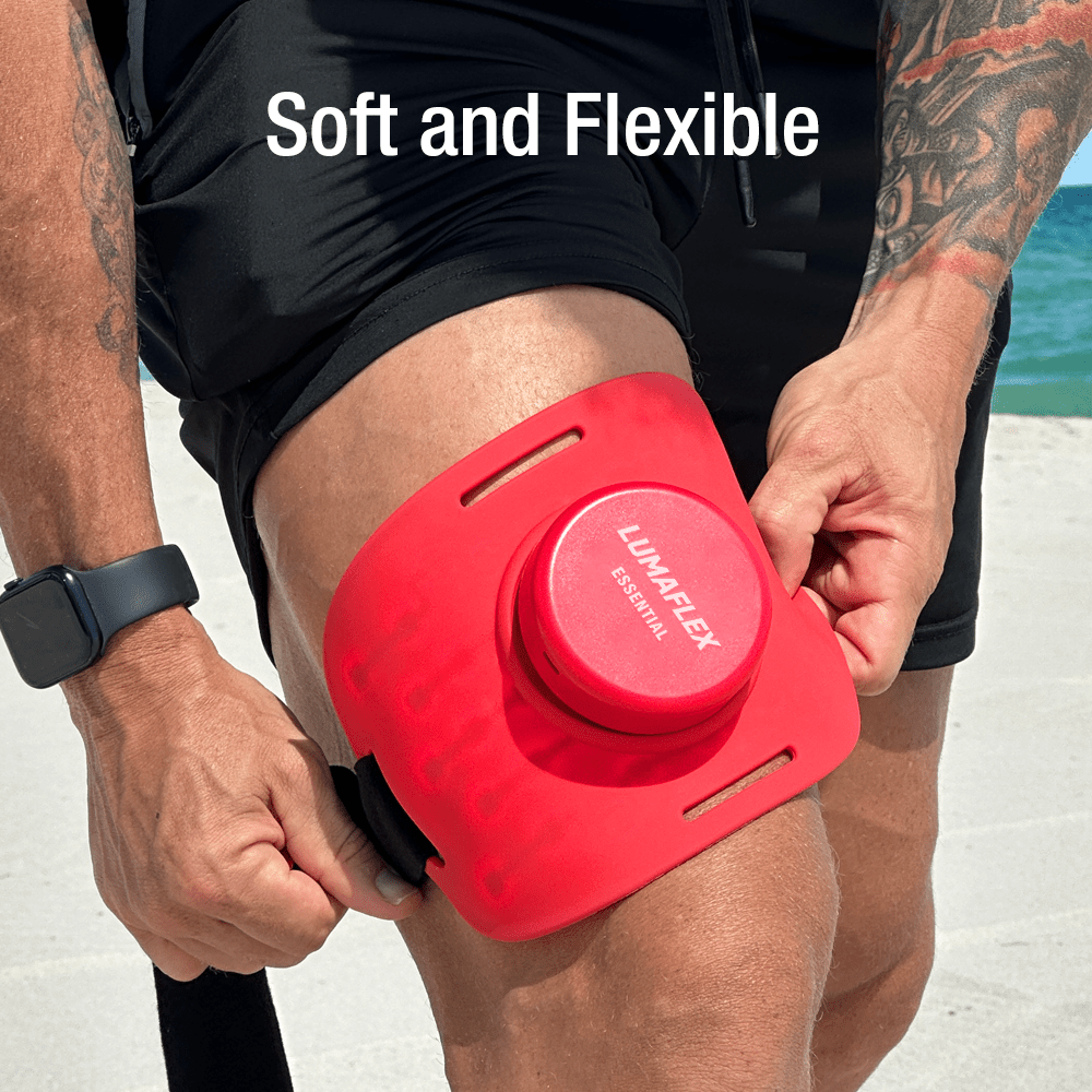 A person in black shorts secures the iReliev Essential Red Light and Infrared Therapy Wrap with two straps to their upper thigh. The branded wrap stands out by the beach, while “Soft and Flexible” above highlights its comfort.