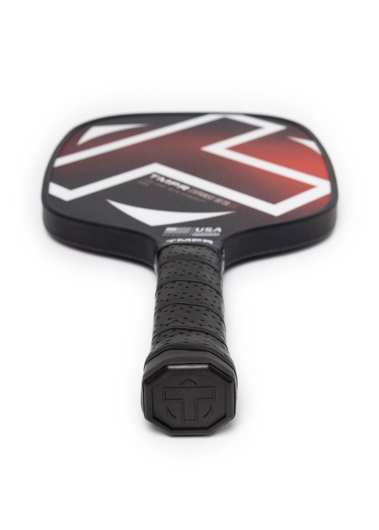 A TMPR Sports Expanse Beta LX paddle in black with a textured grip and bold geometric red, white, and black design on its fiberglass face is shown handle-side on a white background. The hexagonal logo at the handle end highlights spin control.