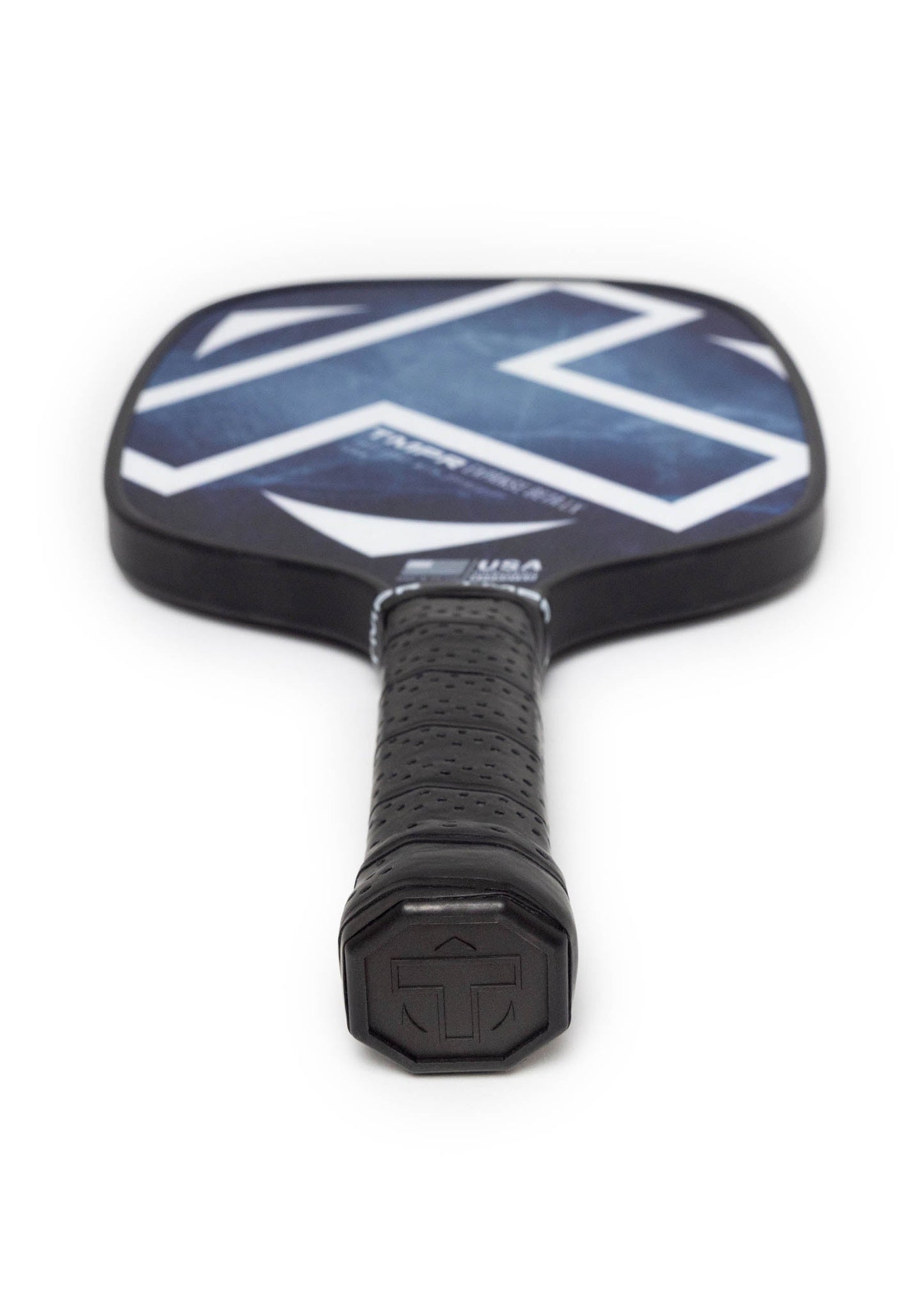 A close-up of the TMPR Sports Expanse Beta LX | Indigo Ice pickleball paddle, showing its textured black grip and a bold blue and white geometric SPINGRIP face for extra power and spin, set against an uncluttered white background.