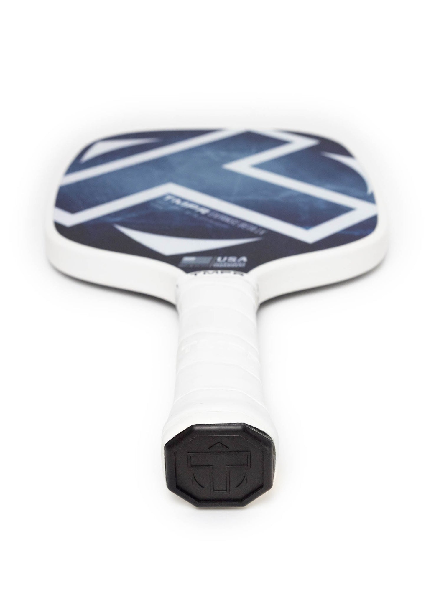 A close-up of the TMPR Sports Expanse Beta LX | Indigo Ice pickleball paddle, viewed from the handle. Its SPINGRIP face boosts power and spin, while a white grip with an arrow and T-shaped logo accents the end cap.