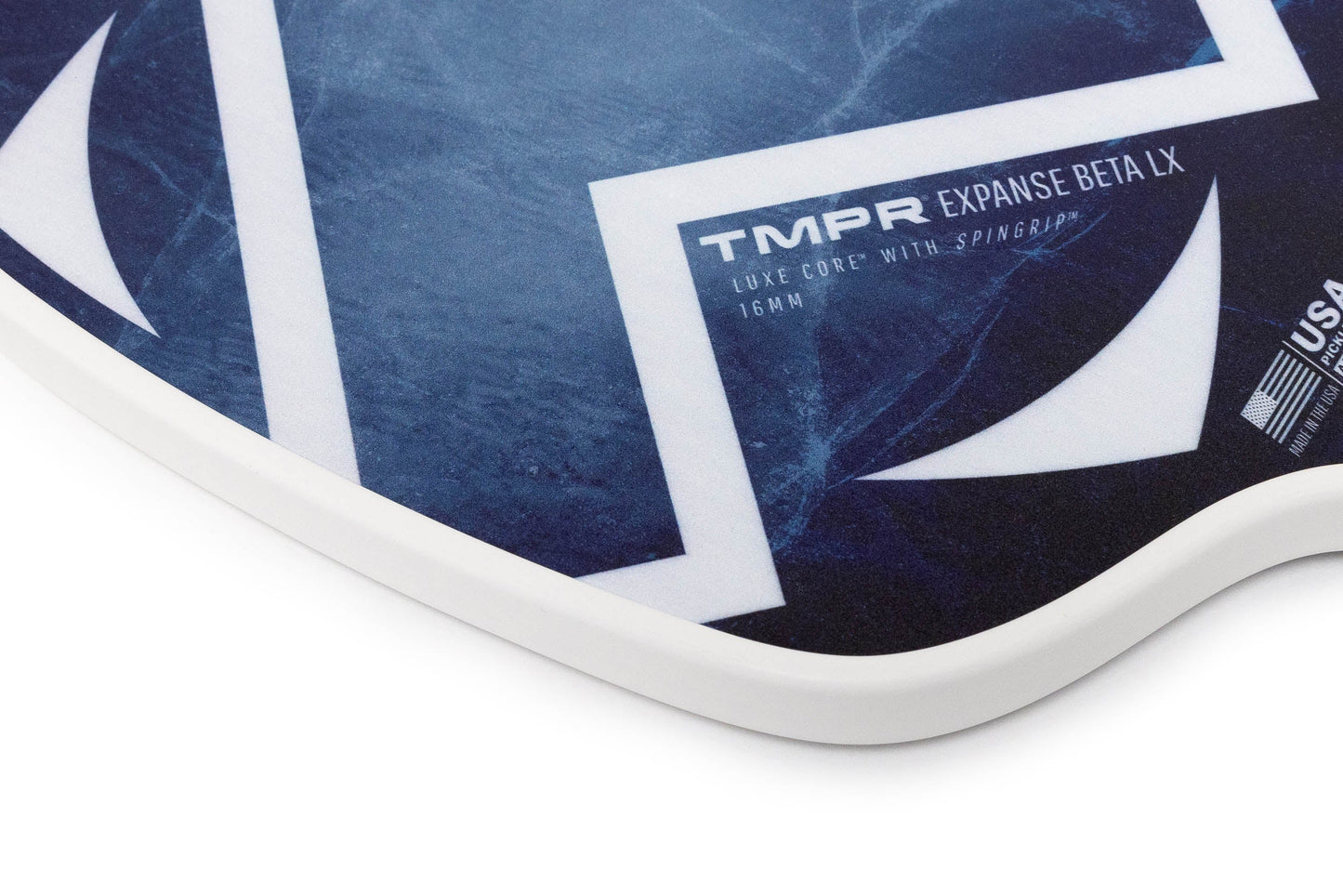 A close-up of the Expanse Beta LX | Indigo Ice paddle from TMPR Sports shows white geometric designs and a SPINGRIP surface for extra power and spin, with “TMPR EXPANSE BETA LX, LUXE CORE with SPINGRIP, 16MM” text and part of a USA Pickleball Approval logo.
