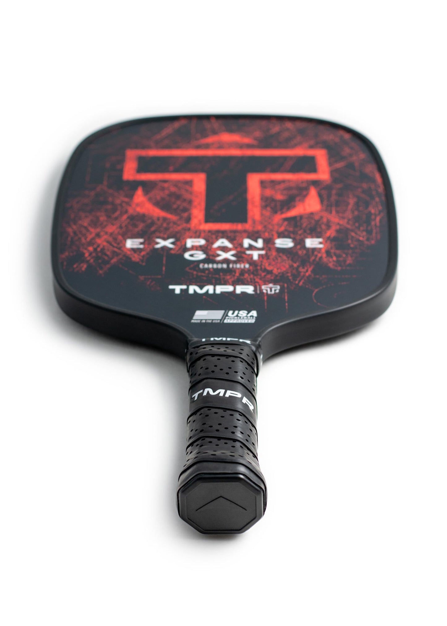 A close-up of the TMPR Sports Expanse GXT carbon fiber pickleball paddle, showcasing its textured black handle, large red “T” logo, and “EXPANSE CARBON” branding on a bold black and red background.