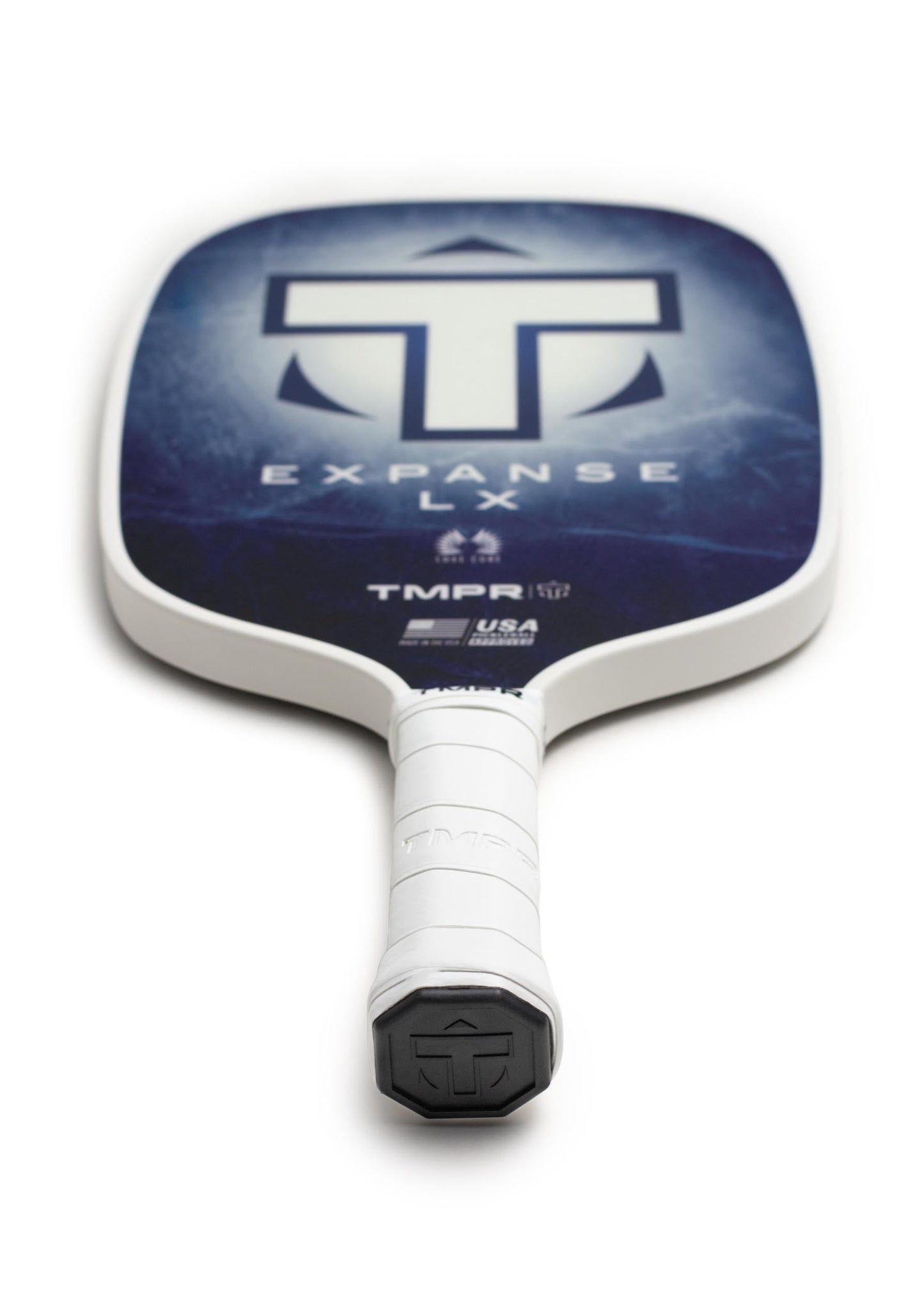 A close-up of the TMPR Sports Expanse LX | Indigo Ice paddle shows its white grip, blue face with bold white T logo, and EXPANSE LX text. The angled view highlights vibration dampening and the handle in the foreground.