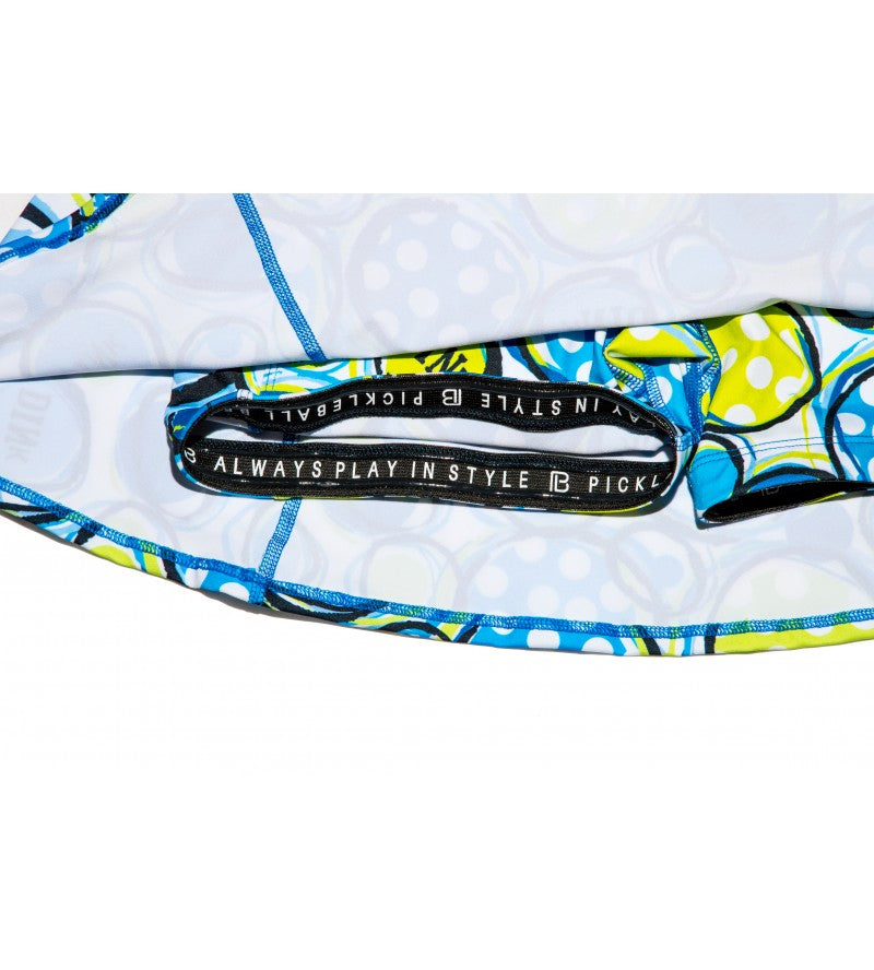 Close-up of Pickleball Bella’s PB Aline Skort Dink 1 fabric bag, featuring a vibrant blue, green, white, and yellow abstract dot pattern and a black zipper pocket with “ALWAYS PLAY IN STYLE PICKLE” in white text.
