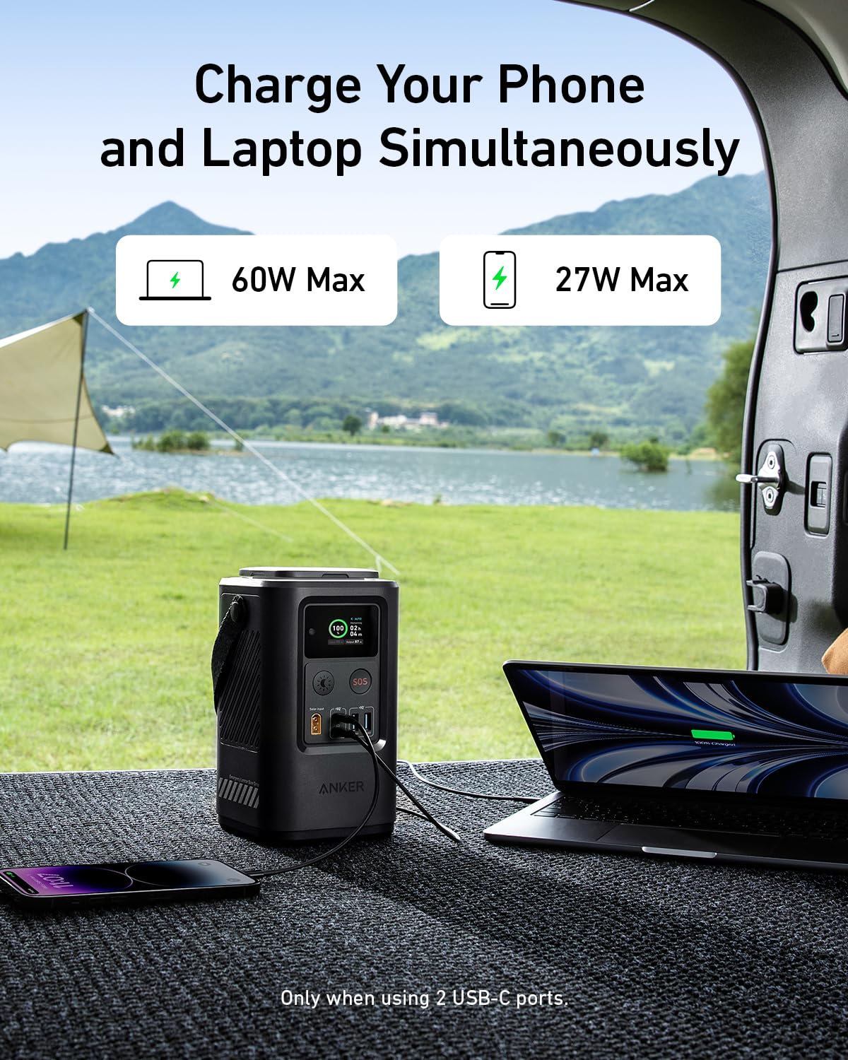 The Anker 548 Power Bank (PowerCore Reserve 192Wh) by Anker charges your phone (max 27W) and laptop (max 60W) at once from a vehicle with its back door open, perfect for outdoor use near green hills and a tent.
