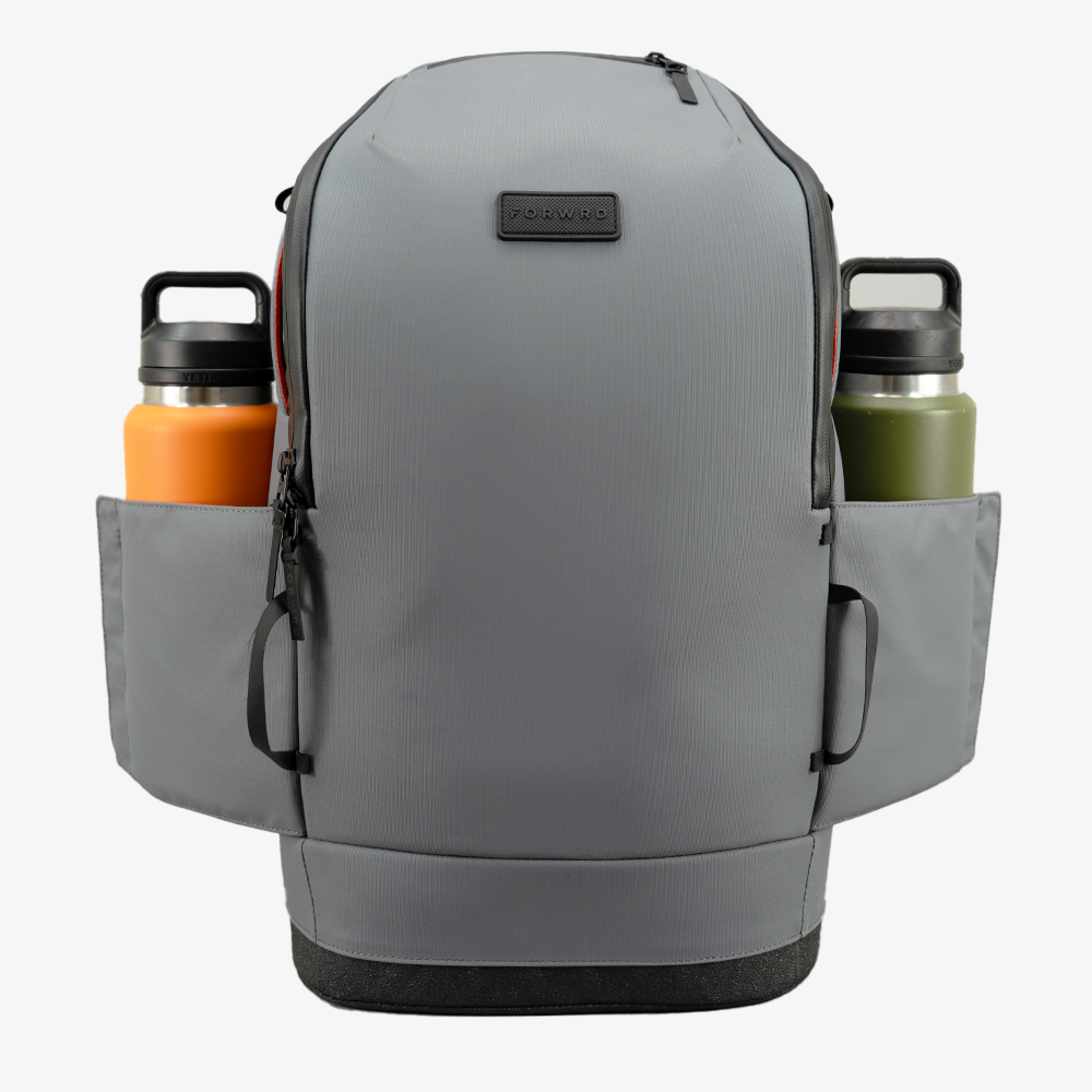 The FORWRD Court Caddy Pickleball Bag in gray features a modular design, front zipper pocket, black bottom panel, two side water bottle pockets (one orange, one green), and a rectangular black logo patch on the top front center.