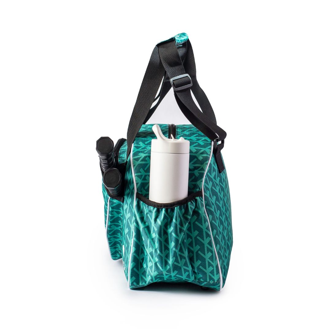 The Pik'le'Ball Sports Court Couture Premium Women's Pickleball Bag with Multiple Compartments and Paddle Sleeve, featuring a teal and white pattern with black straps, stands upright, side view shown with a tumbler and flashlight in front pockets.