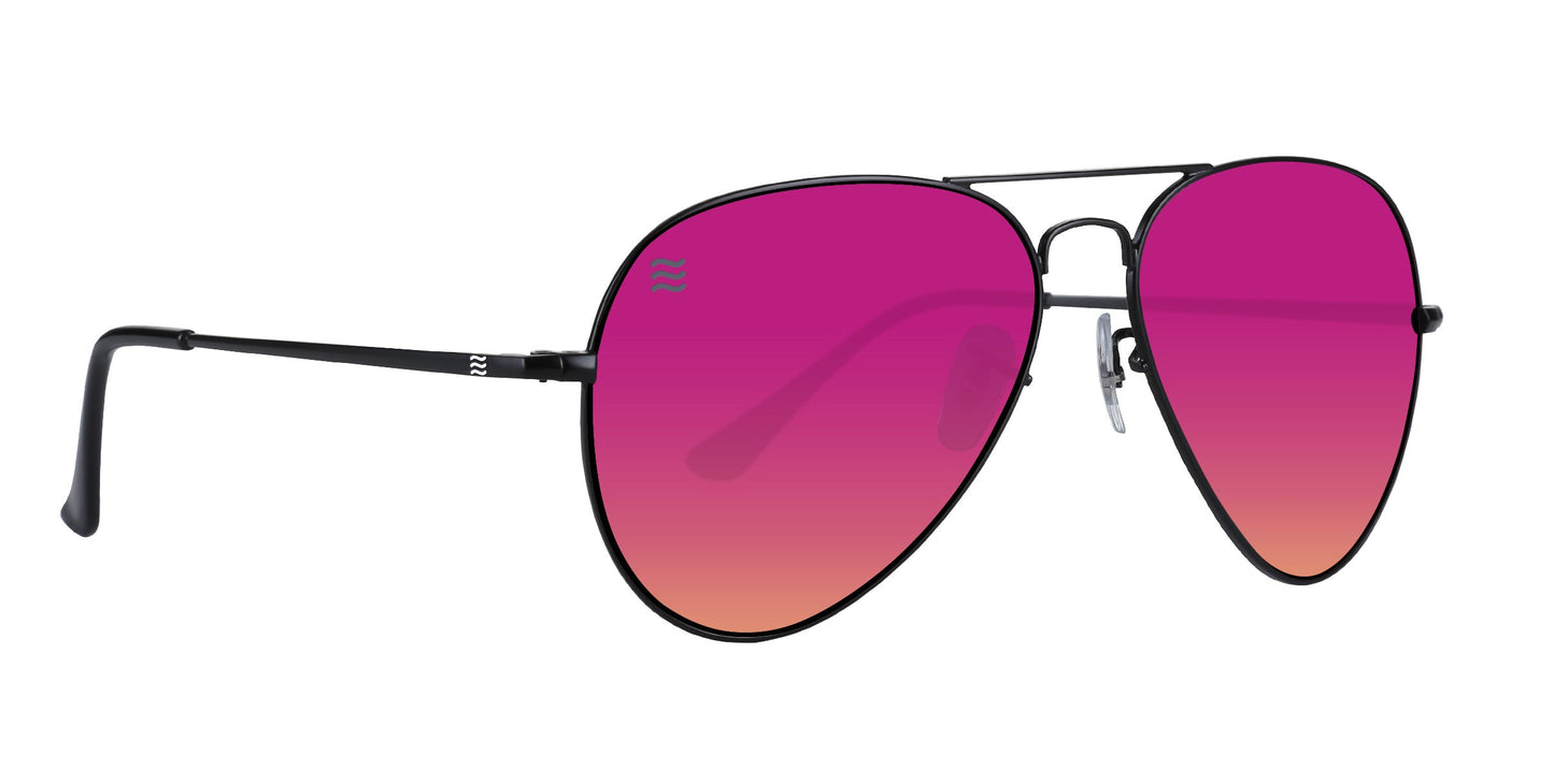 The Space Coast sunglasses by Neven Eyewear feature thin black stainless steel aviator frames and large gradient lenses from bright pink to light orange with a small white wave logo. Left lens offers UV400 protection. Sleek black temples complete the look.