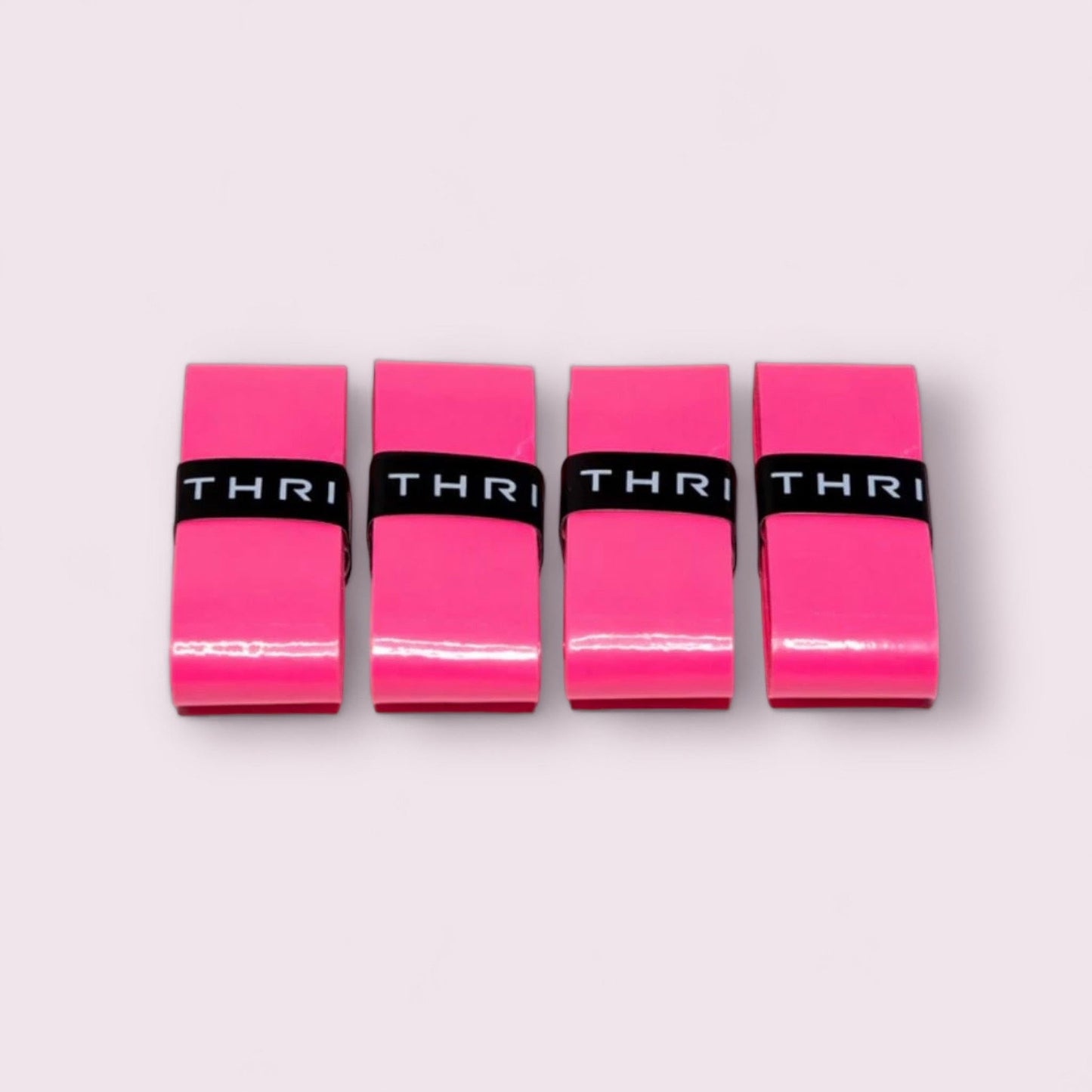 Four bright pink rectangular Overgrips (Super Absorbent) from Thrive Pickleball are lined up side by side on a light pink background, each featuring a black band with "THRI" in white, highlighting the brand and offering a comfortable grip.