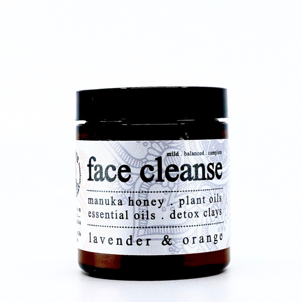 A brown jar from Roots Apothecary labeled "face cleanse" lists manuka honey, plant oils, dead sea salt, essential oils, and detox clays. The scent is lavender & orange. The photo shows a plain white background.