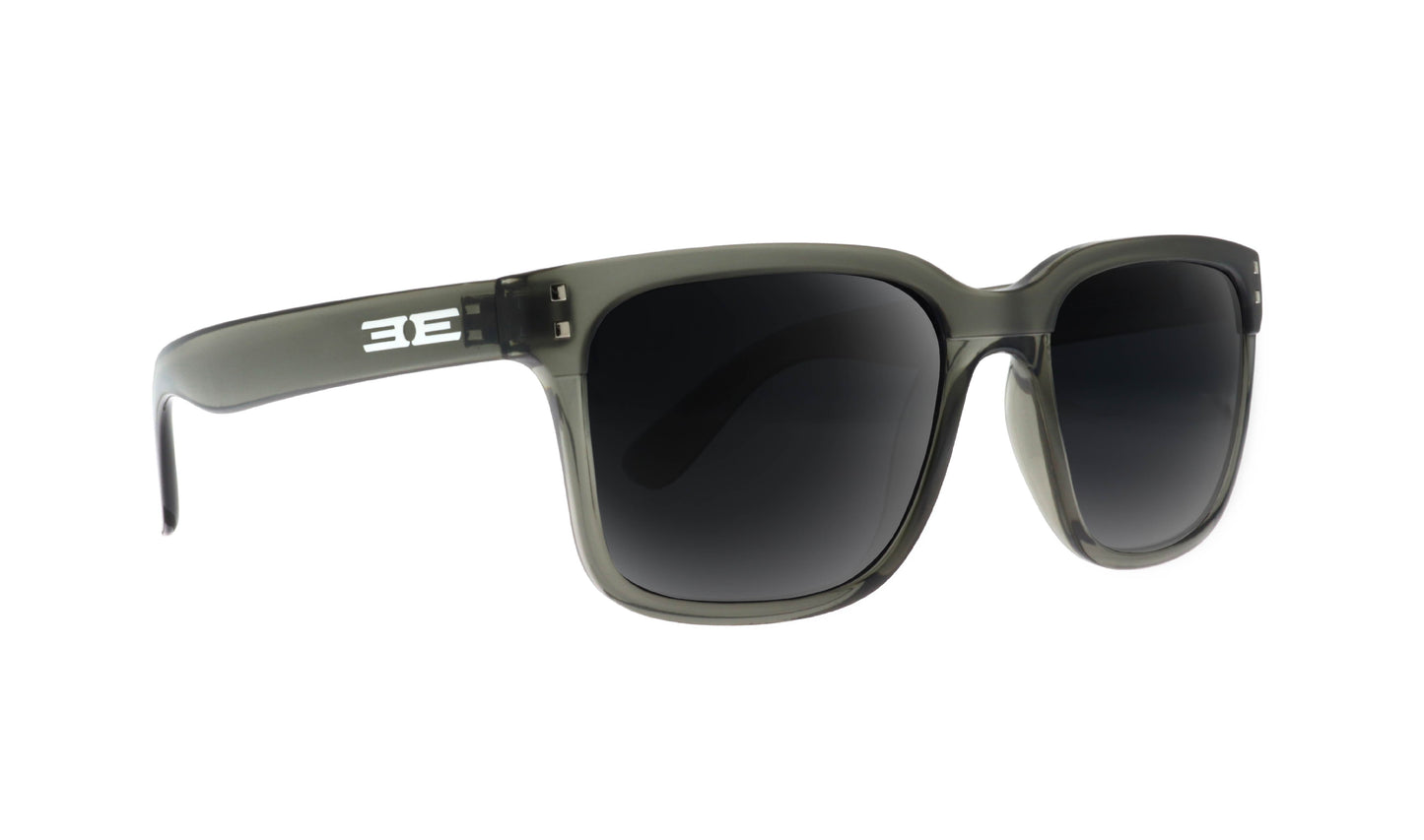 Epoch Eyewear’s Romeo sunglasses are dark, grayish-black full-frame shades with thick translucent plastic frames, black polarized lenses, and a bold white BE logo on the left arm. Displayed on a white background.