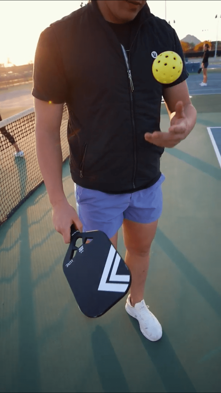 A man holds the LUXE Pickleball Draft paddle, featuring an open throat design, on a tennis court.