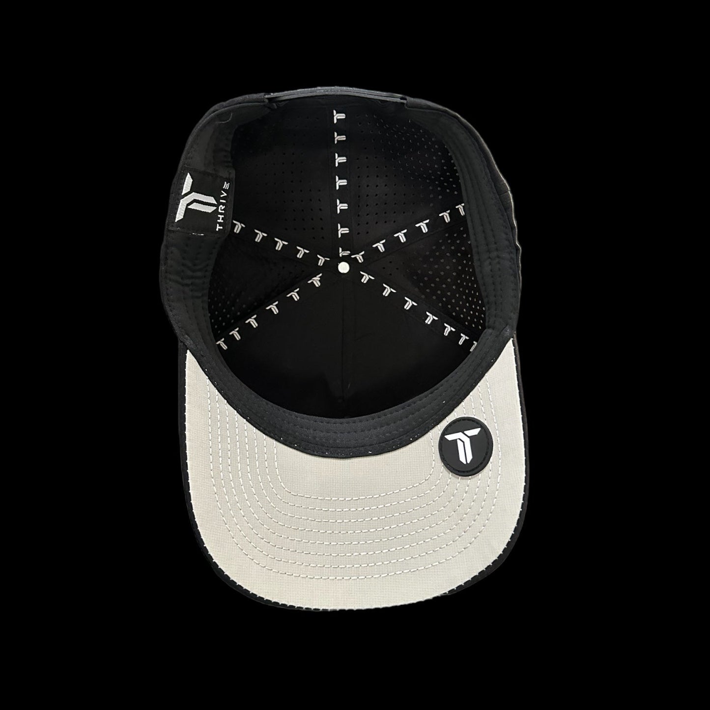 The Thrive Elite Tour Hat by Thrive Pickleball features a white brim with a black and white "T" logo patch, black interior seams with a repeating "T" pattern, and showcases performance headwear design in classic black and white.