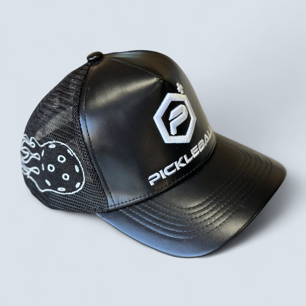 The Potenza Pickleball Leather Logo Trucker Hat features a black leather-like front, mesh back, bold white embroidered PICKLEBALL logo, and flaming pickleball graphic—ideal for fans. Shown on a light gray background.