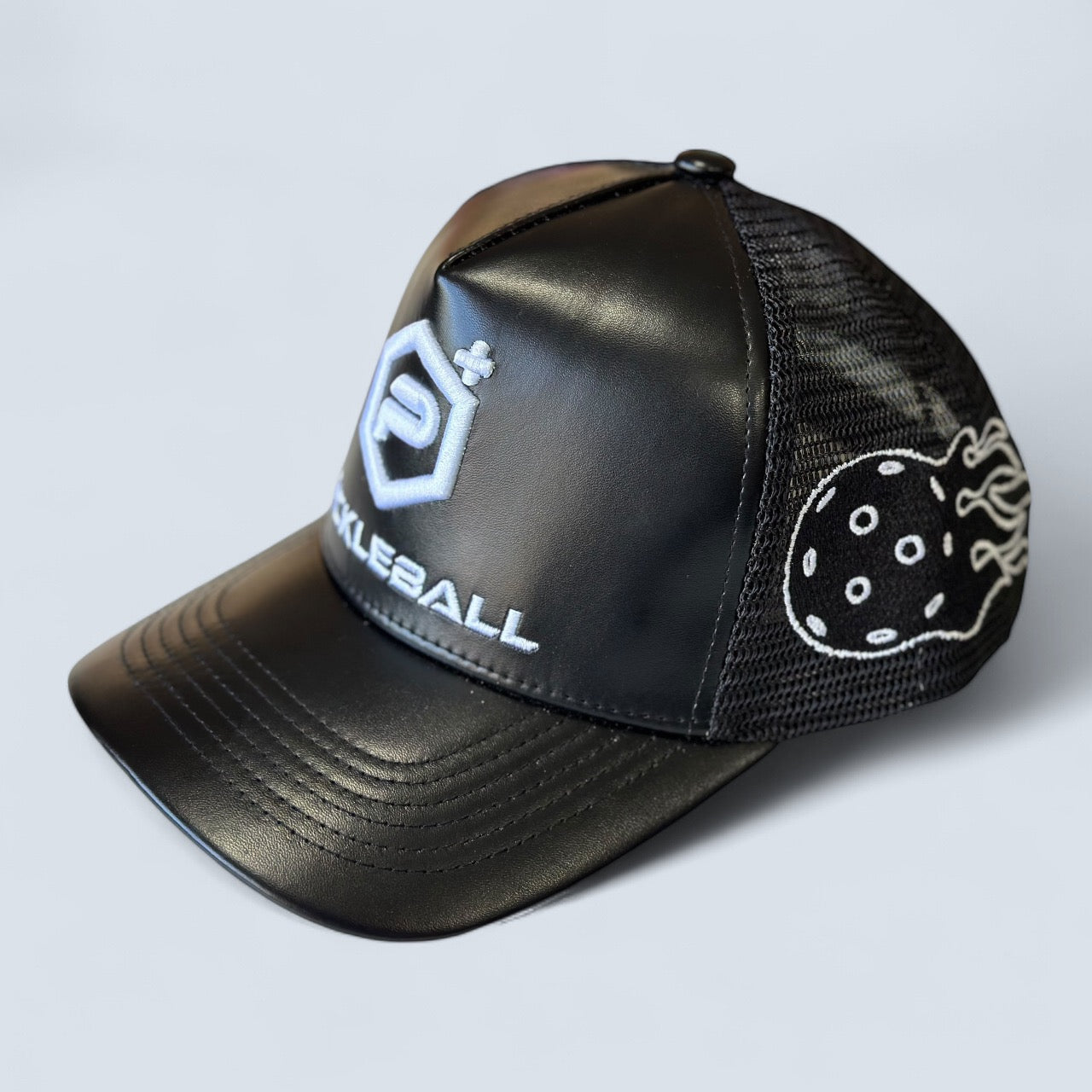 The Leather Logo Trucker Hat by Potenza Pickleball features a black ventilated design with Pickleball and a stylized P logo embroidered in white, plus a mesh side with a flaming pickleball graphic, displayed on a light gray background.
