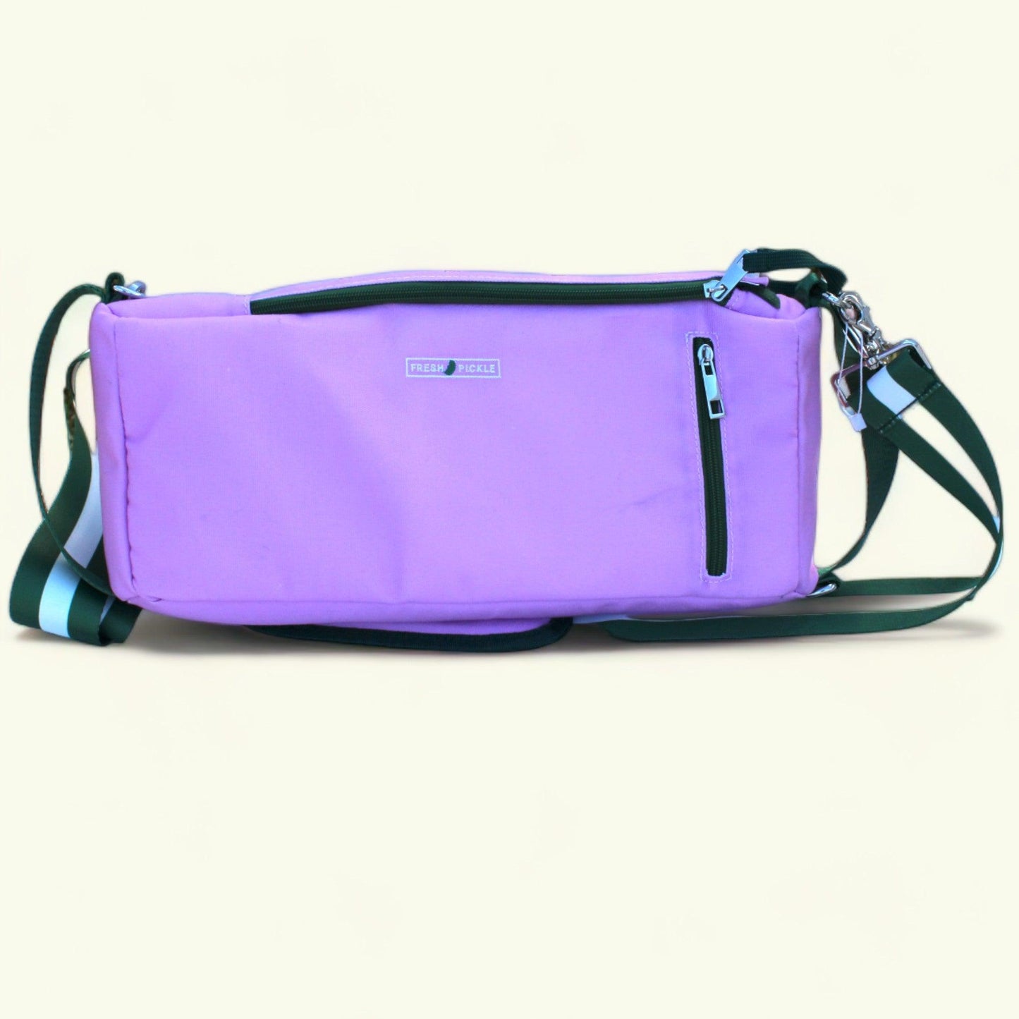 The Fresh Pickle Insulated Cooler Bag is a rectangular lavender crossbody with a black zipper front pocket, small brand label, and adjustable black strap featuring blue and white stripes—ideal for carrying court essentials. Plain off-white background.
