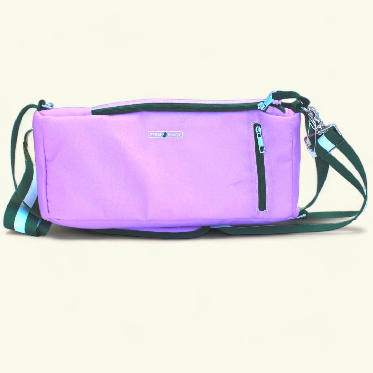 The Fresh Pickle Insulated Cooler Bag features a rectangular lavender design, black front zipper pocket, silver logo tag, turquoise zipper pulls, and an adjustable dark green strap—ideal for carrying court essentials.