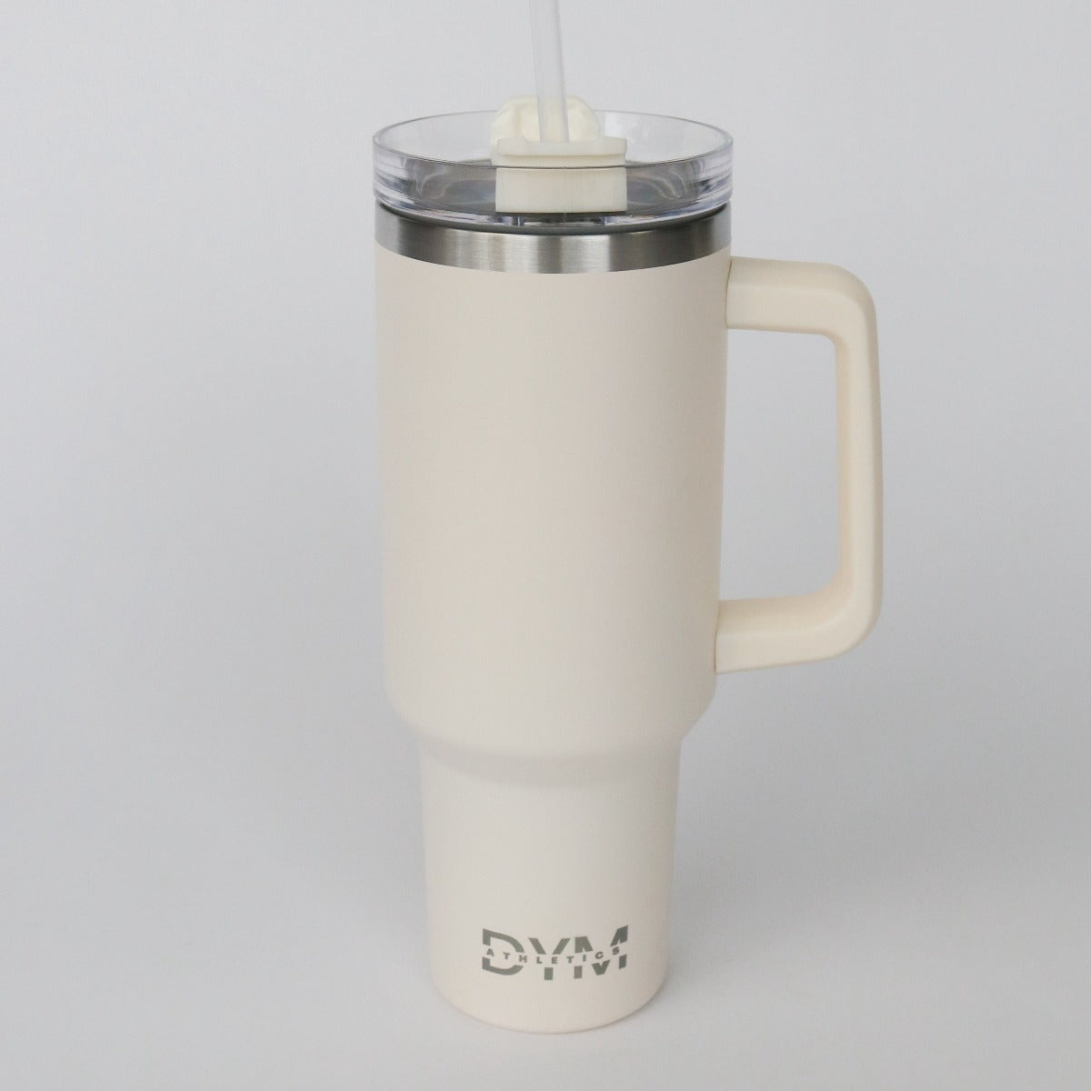 The D.Y.M 40oz Tumbler by DYM Athletics is cream-colored, BPA-free, and fits most car cup holders. It features an ergonomic handle, clear lid with straw, metallic rim, and silver “DYM” logo on the bottom.
