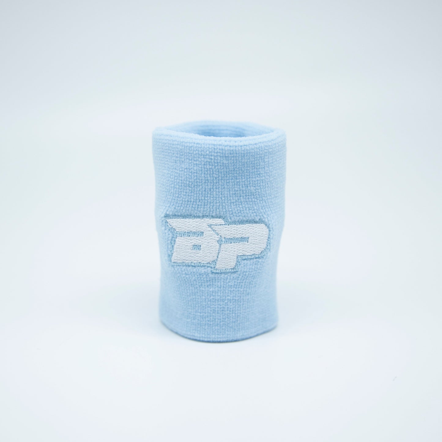 A light blue Bodhi Performance Wristband (1pc) stands upright on a white surface, featuring an embroidered white and gray “DP” logo. Minimal, soft lighting highlights its clean look—perfect as a sweat-wicking pickleball wristband.