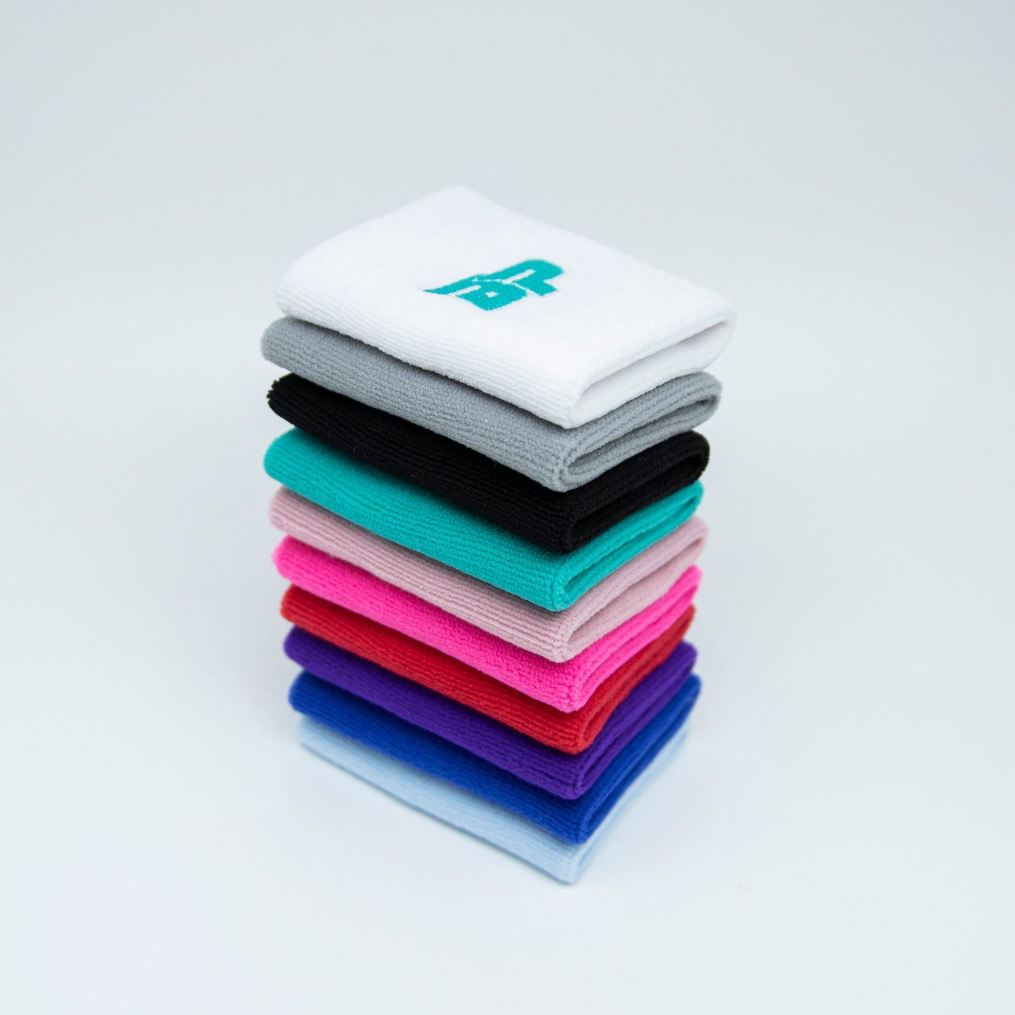 A neatly stacked tower of Bodhi Performance Wristband (1pc) sits on a white surface. These vibrant sweat-wicking bands are ideal for sports like pickleball. The top white band displays a small turquoise embroidered logo.
