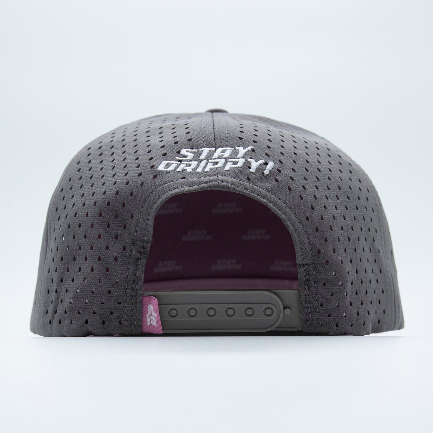 A back view of the Bodhi Performance ICON Snapback in gray shows “STAY GRIPPY!” embroidered in white above the adjustable closure, a pink accent on the strap, and a subtle patterned lining inside.