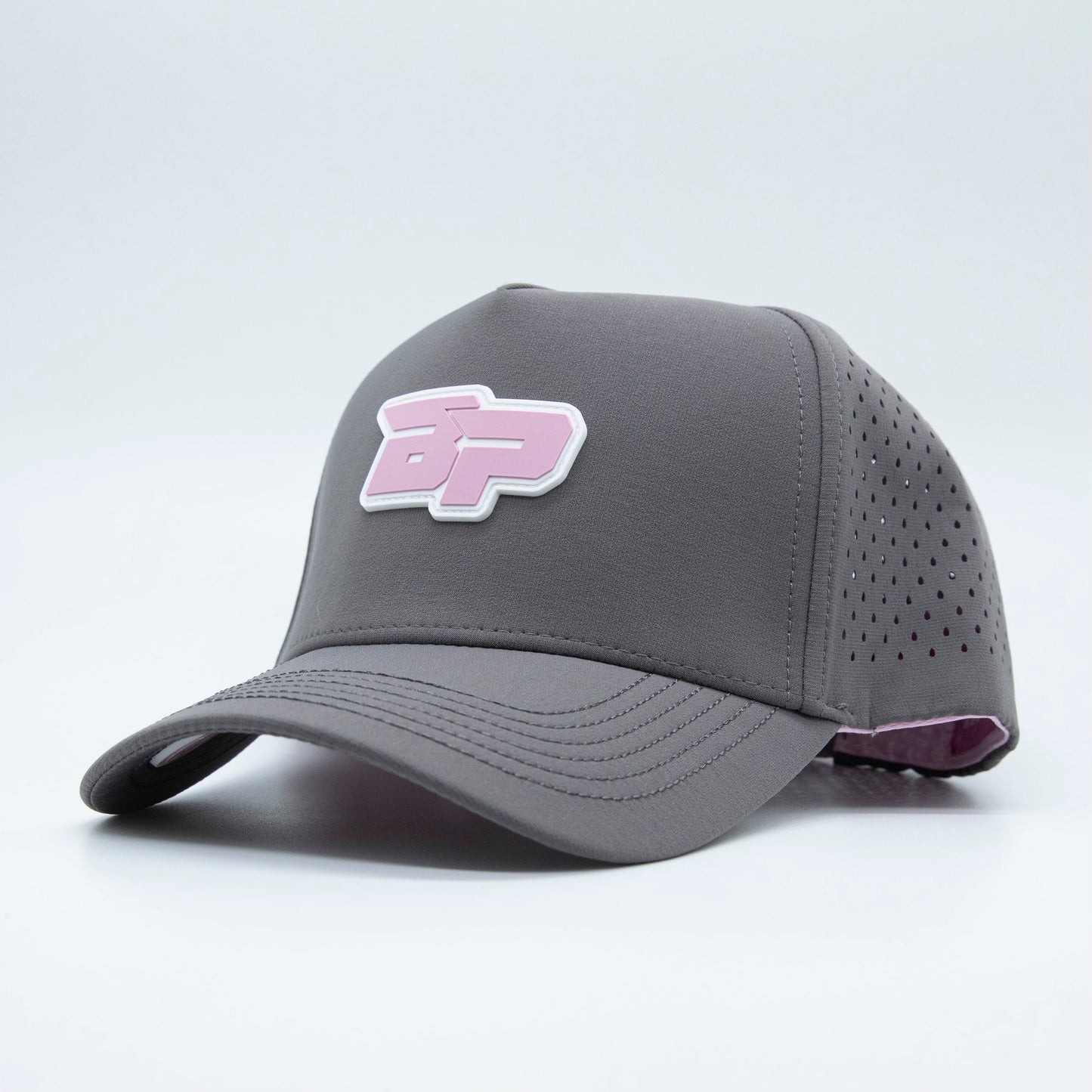 The Bodhi Performance ICON Snapback is a gray pickleball hat with a curved brim, perforated sides, and a raised pink and white "BP" logo. The purple underside and lining add standout style to this performance hat.