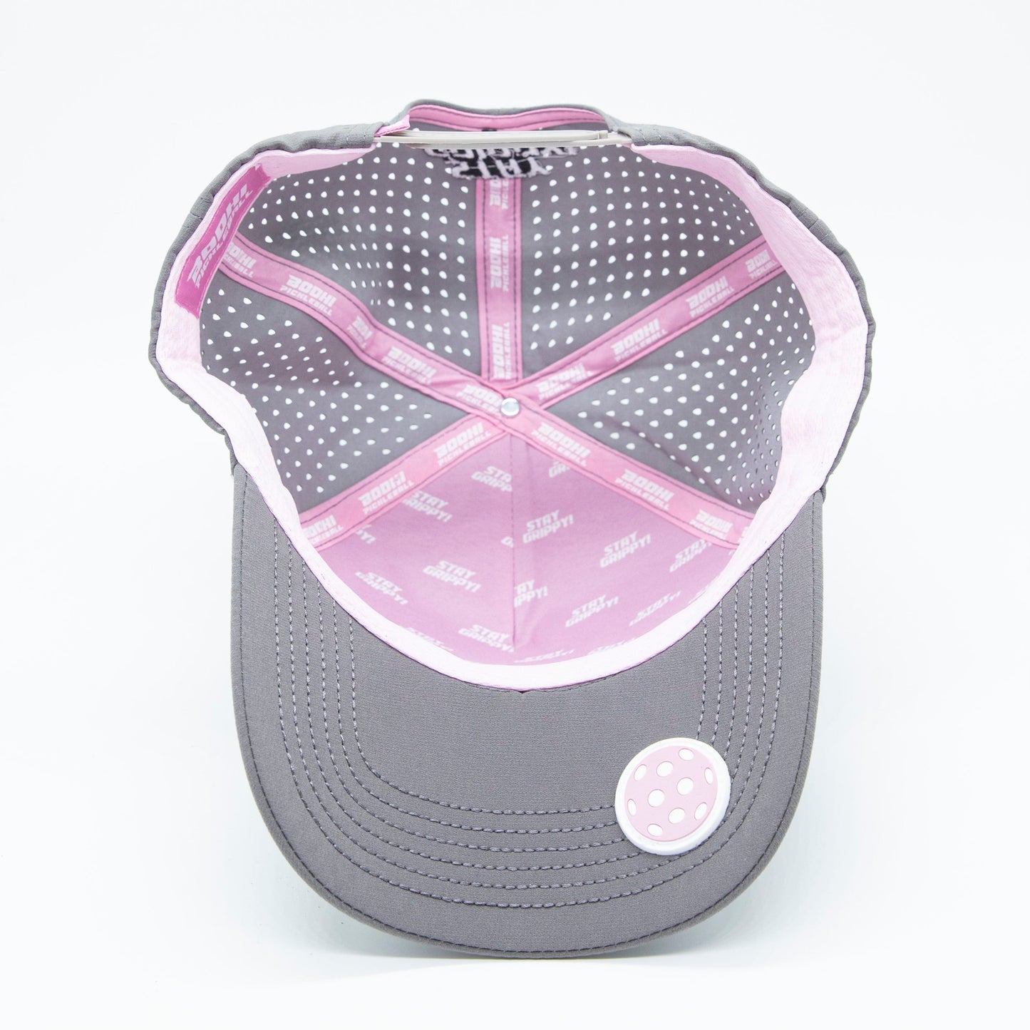 A Bodhi Performance ICON Snapback cap in gray is seen from above, featuring white polka dots, pink trim with white text, reinforced stitching, and a round pink-and-white ventilation patch on the brim against a white background.