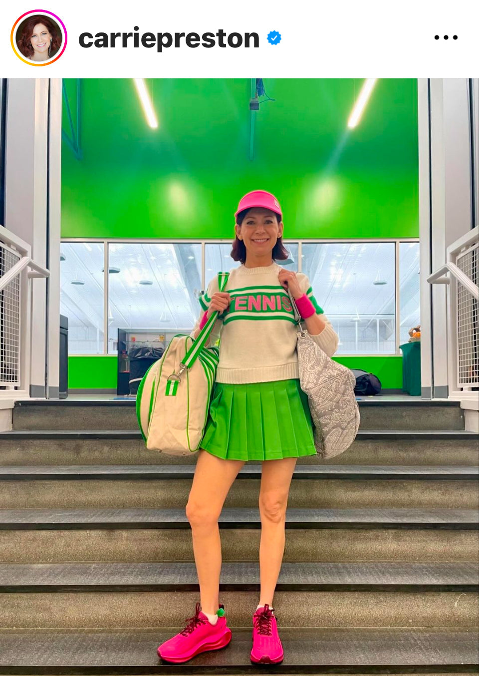 A woman stands indoors on steps, smiling in the Runway Athletics TENNIS SWEATER (Off White, Green, Pinke) and matching skirt, with a pink cap and sneakers. She holds two bags as glowing lights brighten the green backdrop. Instagram interface visible.
