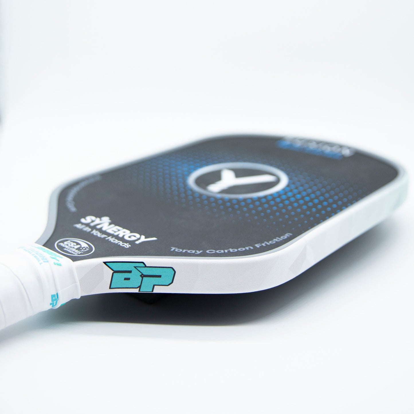 A close-up of Bodhi Performance Premium Edge Tape - PATTERNS on a black paddle with a blue BP logo. The plain white background highlights the stylish edge tape, showcasing durability and premium protection for pickleball equipment.