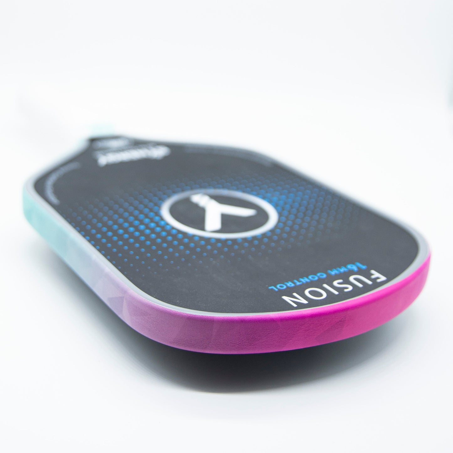 A close-up of a pickleball paddle on a white surface, featuring a black face with blue dots, a central white logo, and pink-to-blue Bodhi Performance Premium Edge Tape - PATTERNS along the edge for protection. The word FUSION is visible.