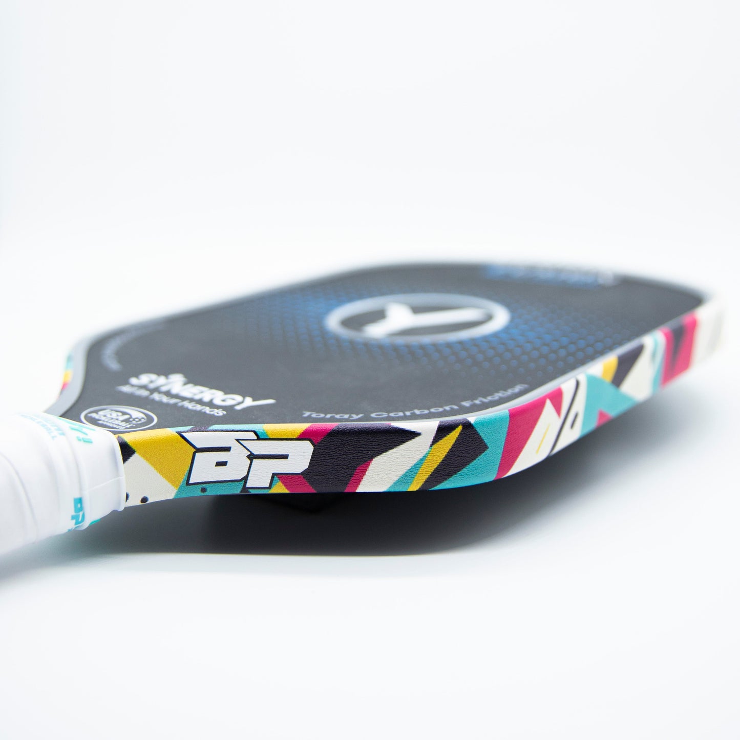 A close-up of Bodhi Performance’s Premium Edge Tape - PATTERNS, featuring a vibrant geometric design on the edge of a pickleball paddle with a white handle and textured black surface, placed on a clean white background.