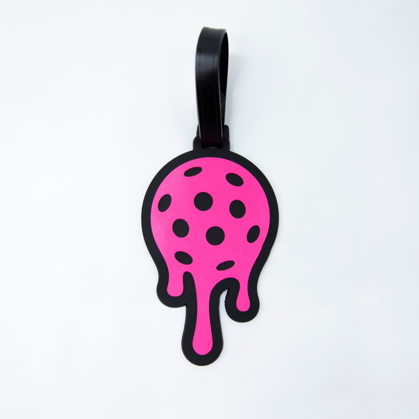 The Bodhi Bag Tags by Bodhi Performance feature a bright pink, round design with black polka dots, bold outline, and three drip-like extensions. With a black strap, they're fun pickleball accessories—perfect as tags for your pickleball bag.