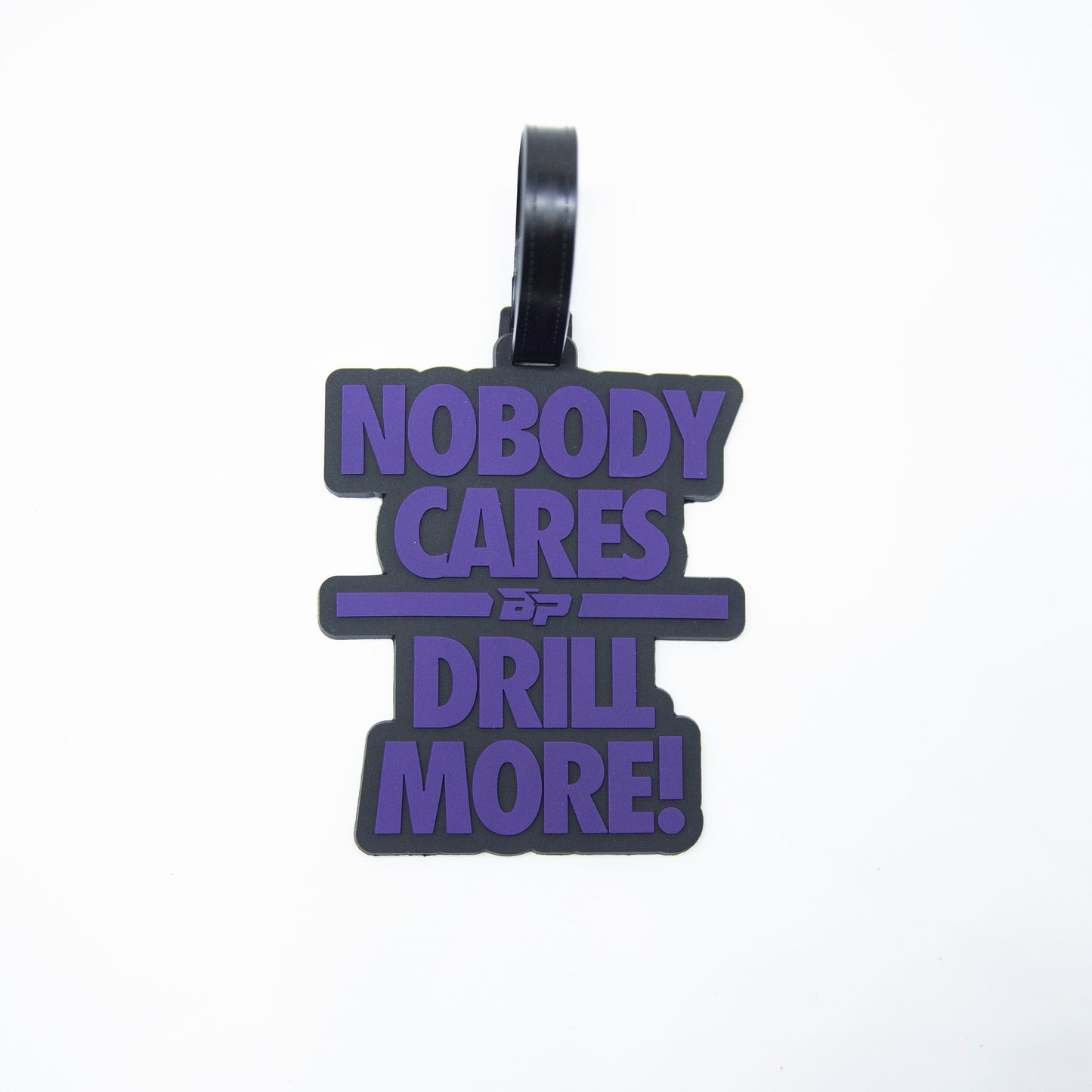 The Bodhi Bag Tags by Bodhi Performance are black keychain tags with bold purple "NOBODY CARES DRILL MORE!" text, striking lines, a double “D” logo in the center, and a black loop—ideal as a pickleball or tournament bag tag.