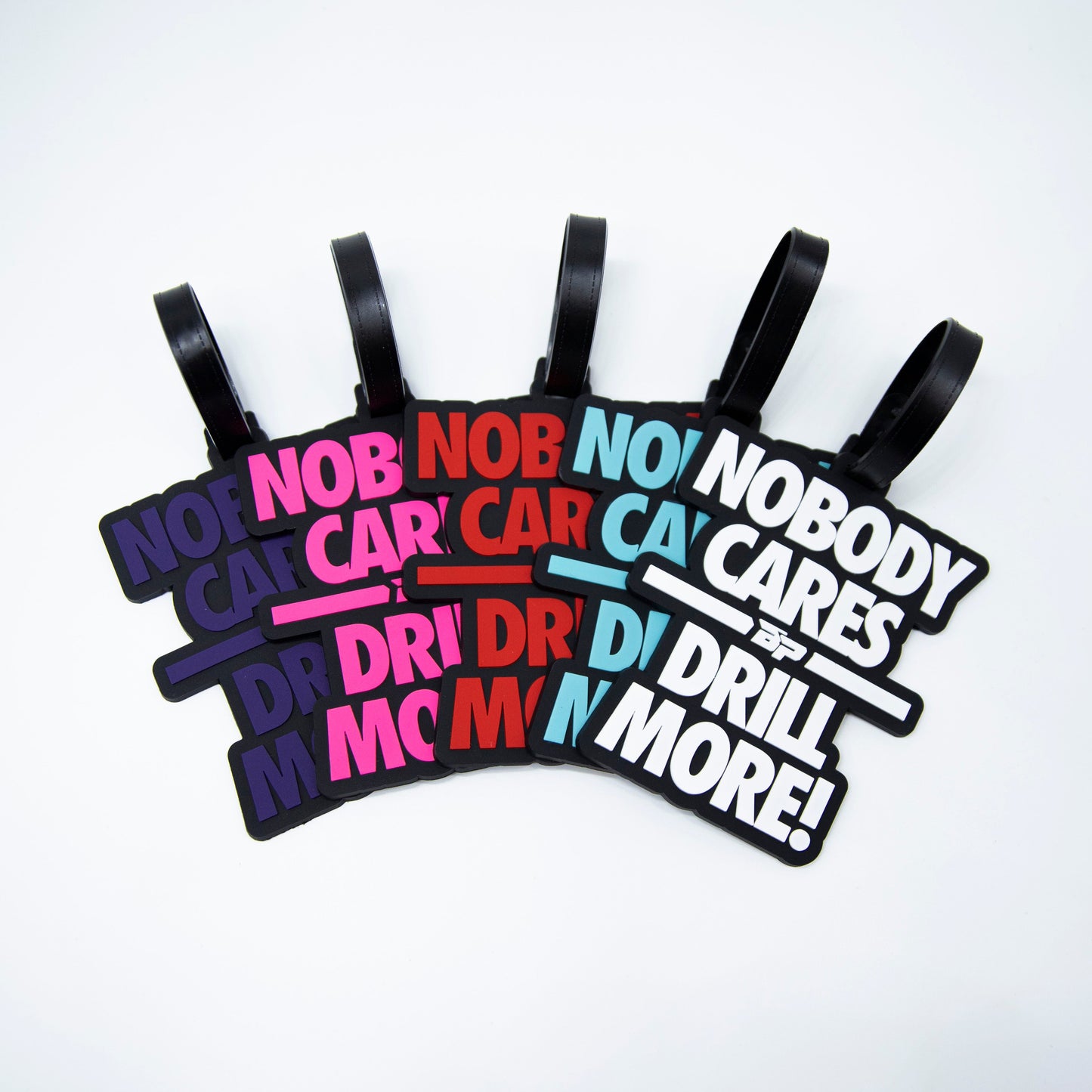 Five Bodhi Bag Tags by Bodhi Performance are shown in a fan layout, each with “NOBODY CARES, DRILL MORE!” in bold and different colors. These tournament tags include black straps for easy attachment.