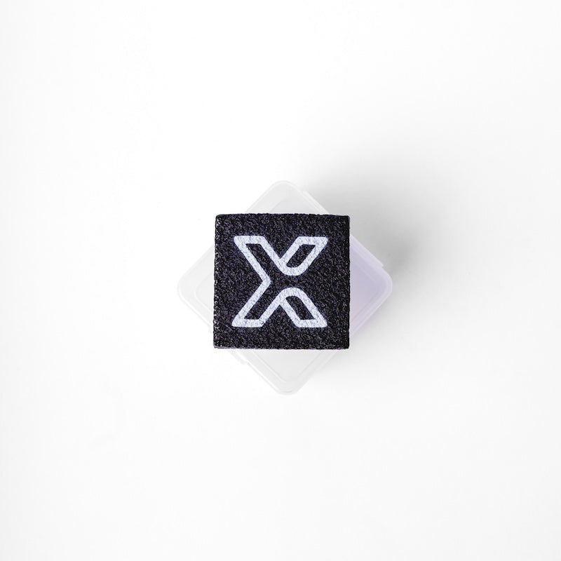 The body helix Pickleball Paddle Eraser and Refresher, a black square eraser with a bold white “X”, rests on a translucent plastic box, photographed from above on a plain white background, ready for paddle maintenance.