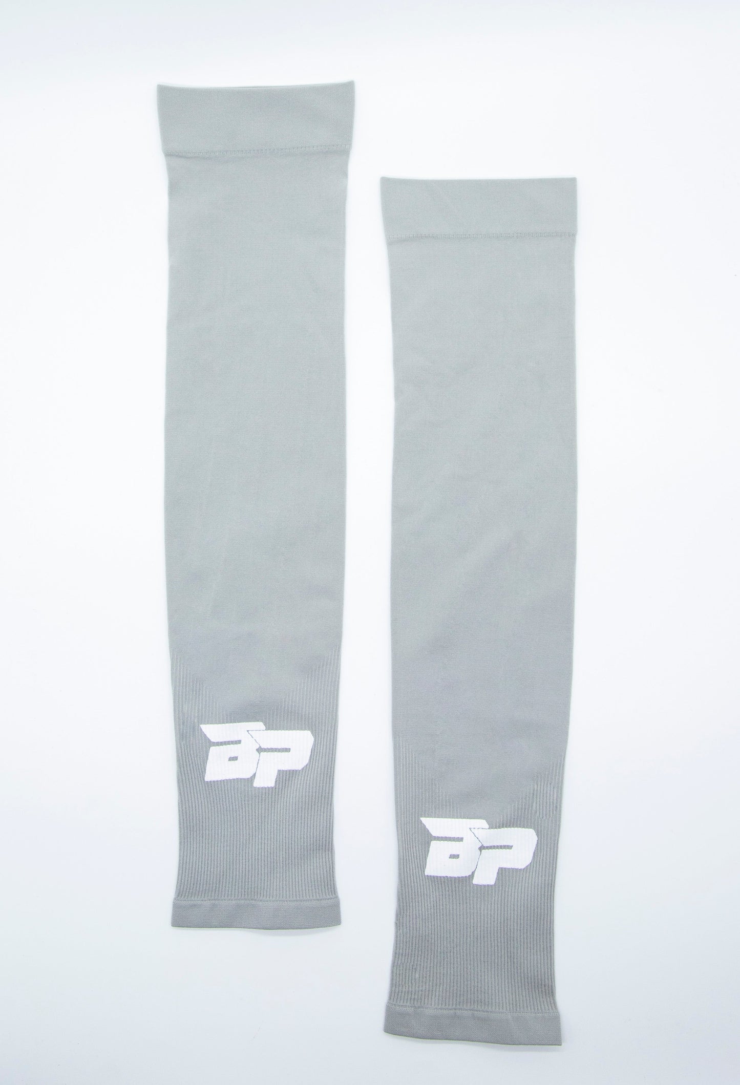 Two Bodhi Performance Arm Sleeves in gray fabric are laid flat on a white surface. Each sleeve features a white BP logo near one end; they are identical in design and color, with one slightly longer than the other.