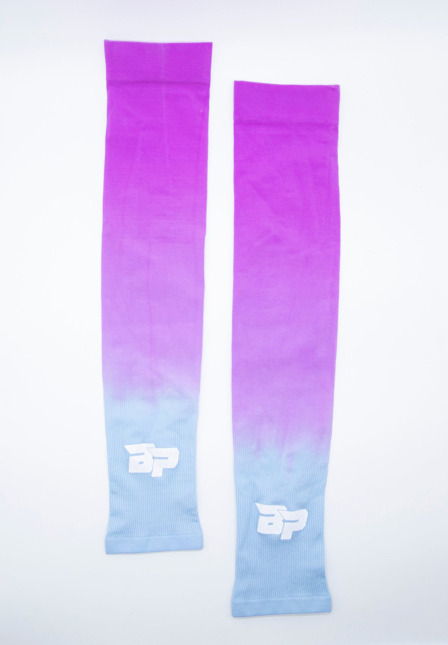 Two Bodhi Performance Arm Sleeves are laid flat on a white background. Each moisture-wicking sleeve fades from bright pink to light blue, featuring a white, stylized BP logo near the blue end.