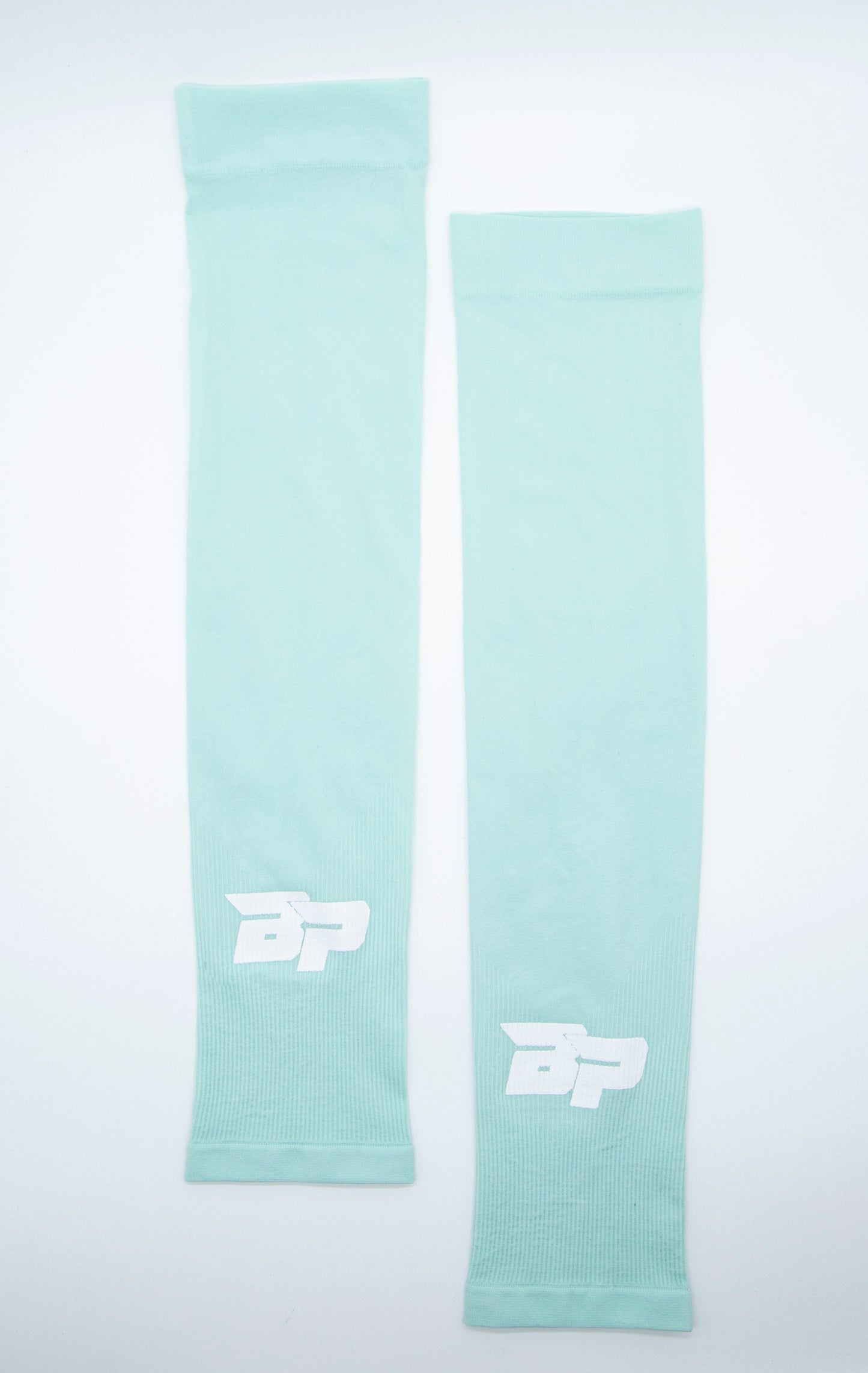 Two light teal Bodhi Performance Arm Sleeves are laid flat on a white background, each with a white stylized "BP" logo near the wrist. The simple, stretchy sleeves are made of smooth athletic fabric.
