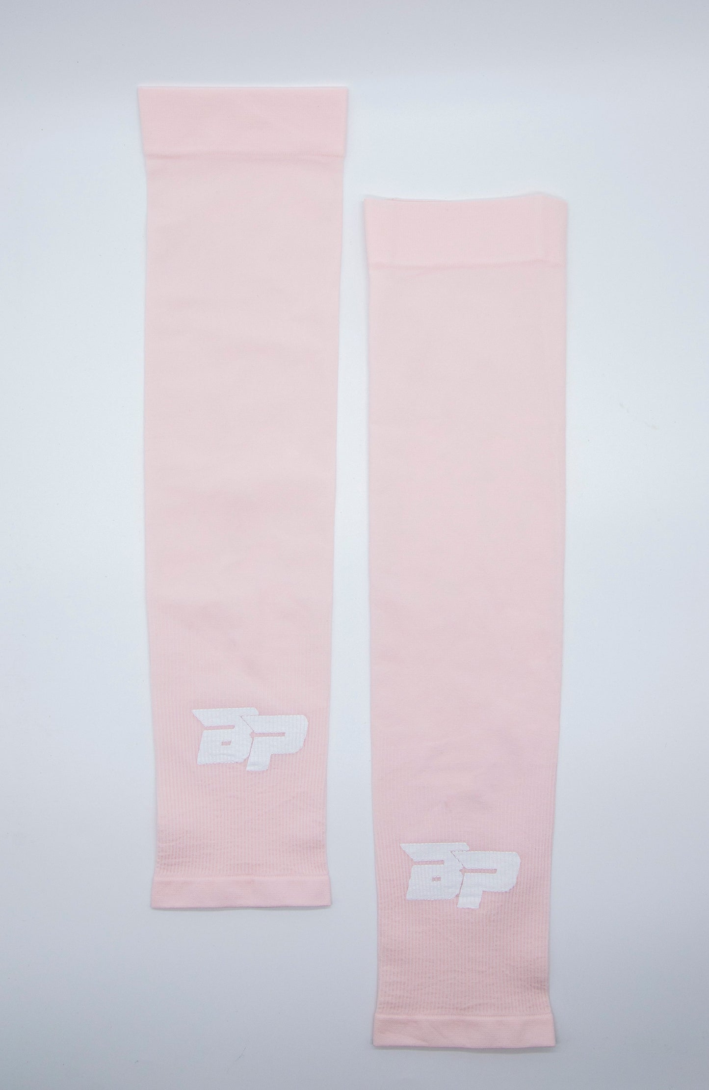 Two light pink Bodhi Performance Arm Sleeves are laid flat on a white background, each with a white stylized BP logo near the cuff. Made from smooth, stretchy, moisture-wicking material, these sleeves are perfect for athletic use.