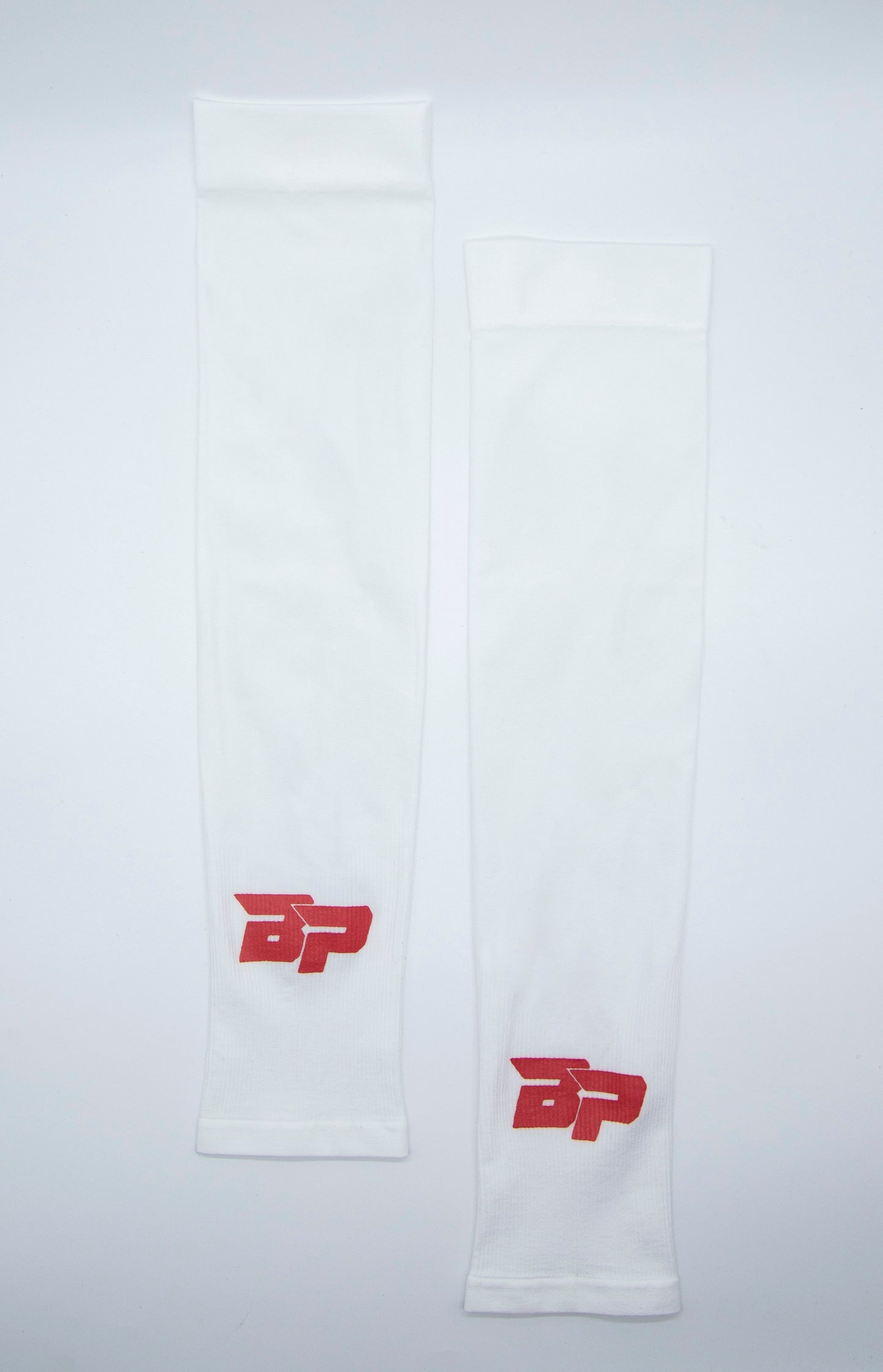 Two Bodhi Performance arm sleeves are laid flat and parallel on a white background. Both white Performance Arm Sleeves feature a red BP logo near the wrist, appearing clean, smooth, and identical in design.