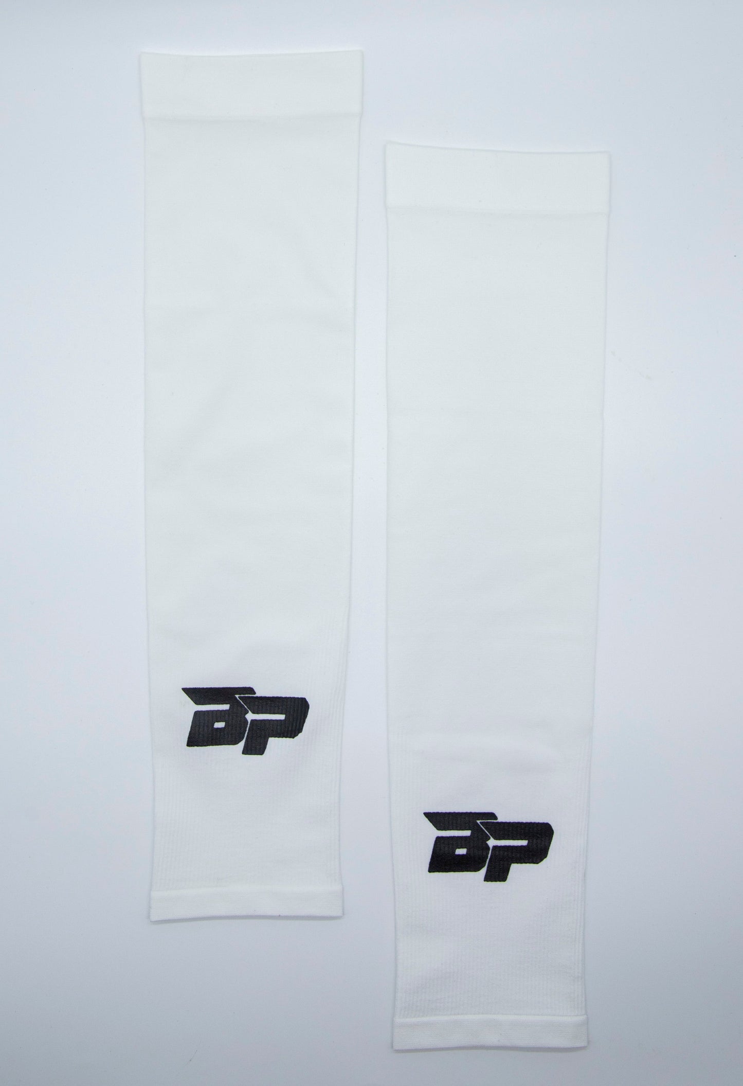 Two white Bodhi Performance Arm Sleeves are laid flat, each featuring a black BP logo near one end. Made from smooth, stretchy material, these sleeves are designed for athletic use and provide moisture-wicking comfort.