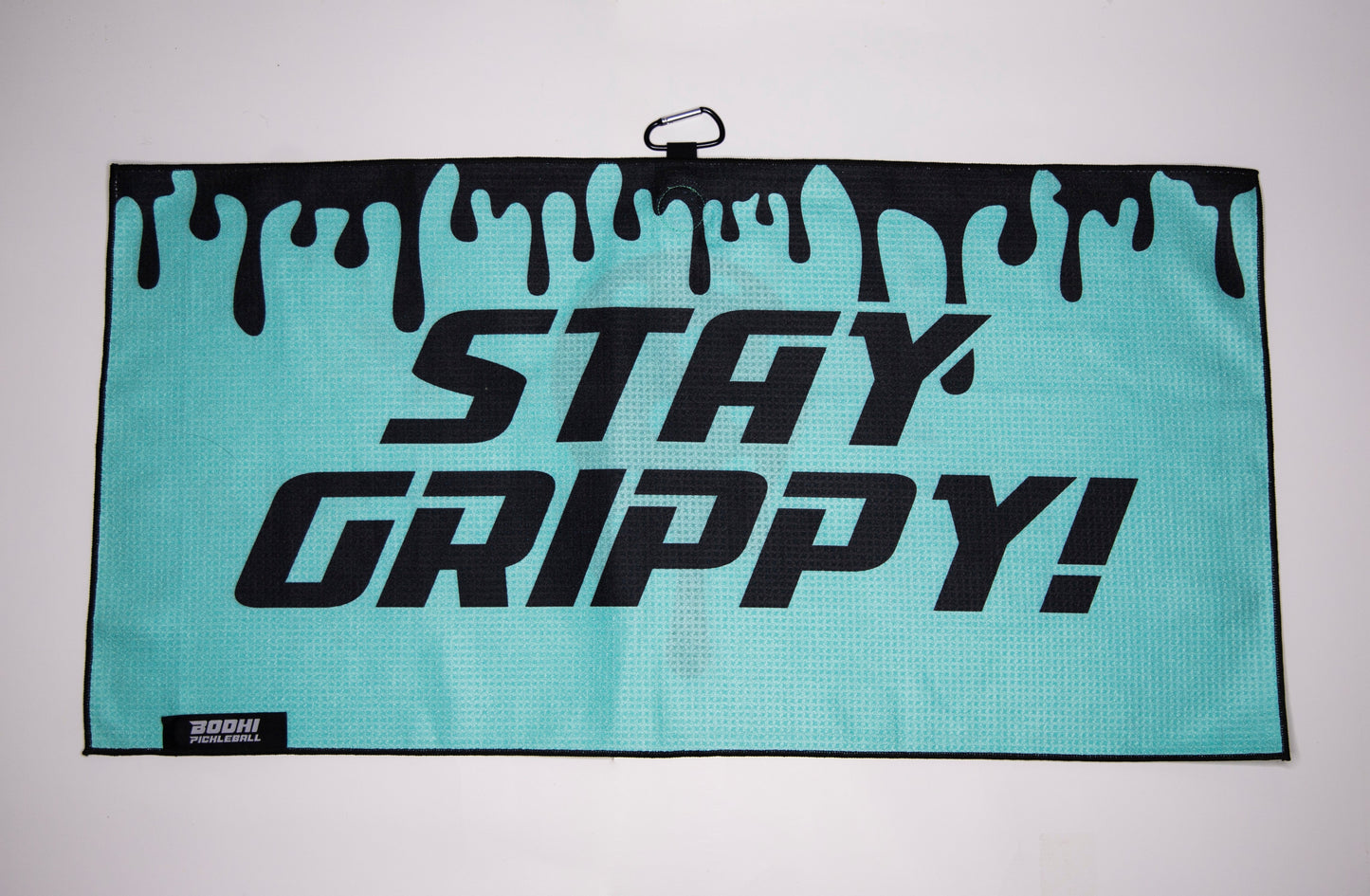 The Bodhi Performance Pickleball Towel is a rectangular teal microfiber towel featuring a black dripping paint design on top, bold "STAY GRIPPY!" text, a small top hook, and the Bodhi Performance logo—an essential pickleball accessory.