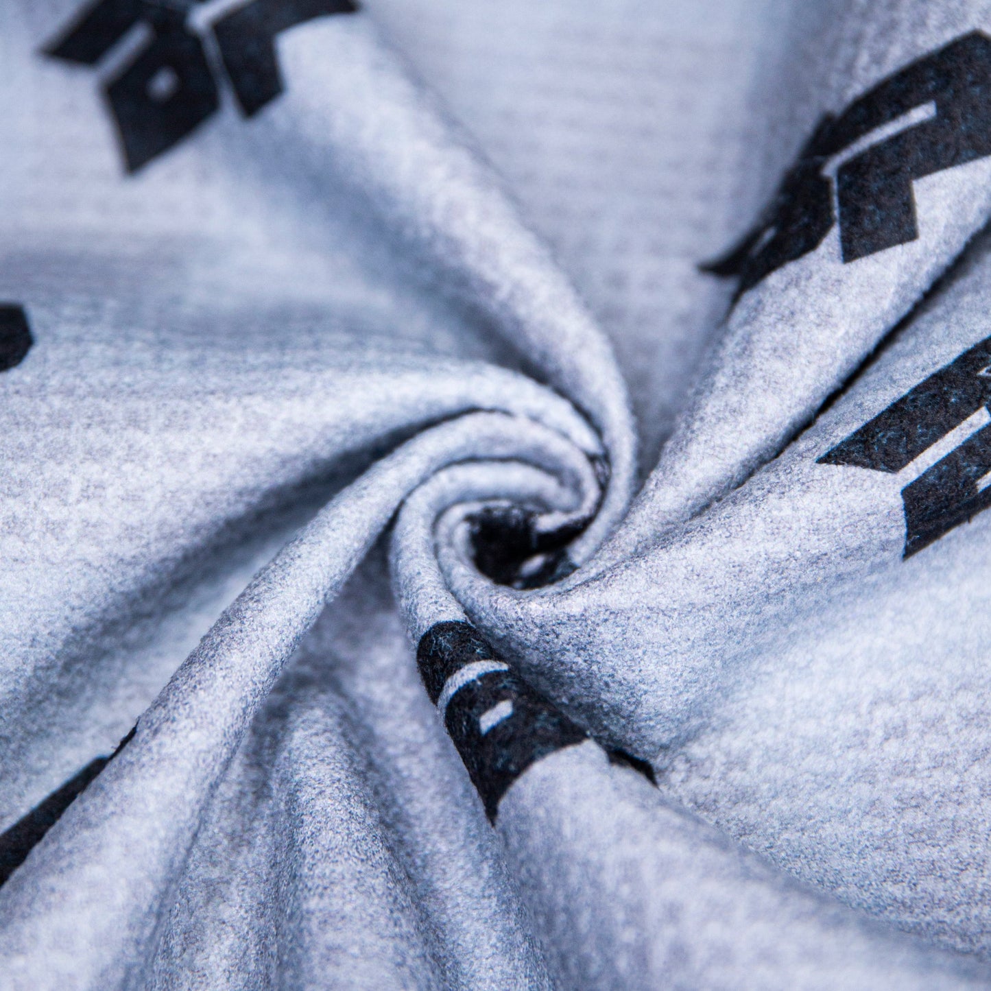 Close-up of the Bodhi Performance “Performance Pickleball Towel” in light gray microfiber, twisted to highlight its detailed fibers and dynamic black geometric patterns—an eye-catching pickleball accessory.